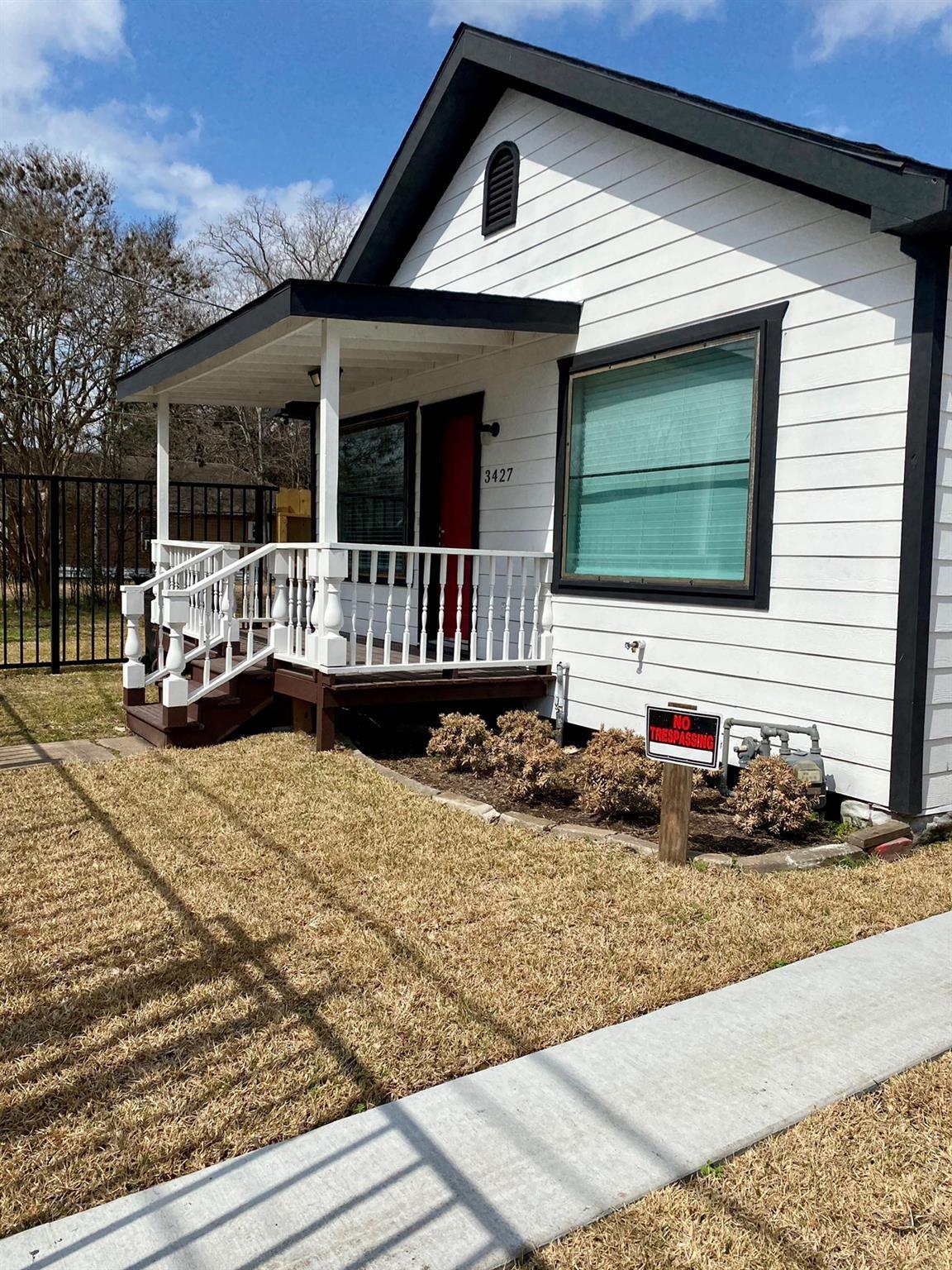 White house with dark trim, red front door, and raised covered porch.