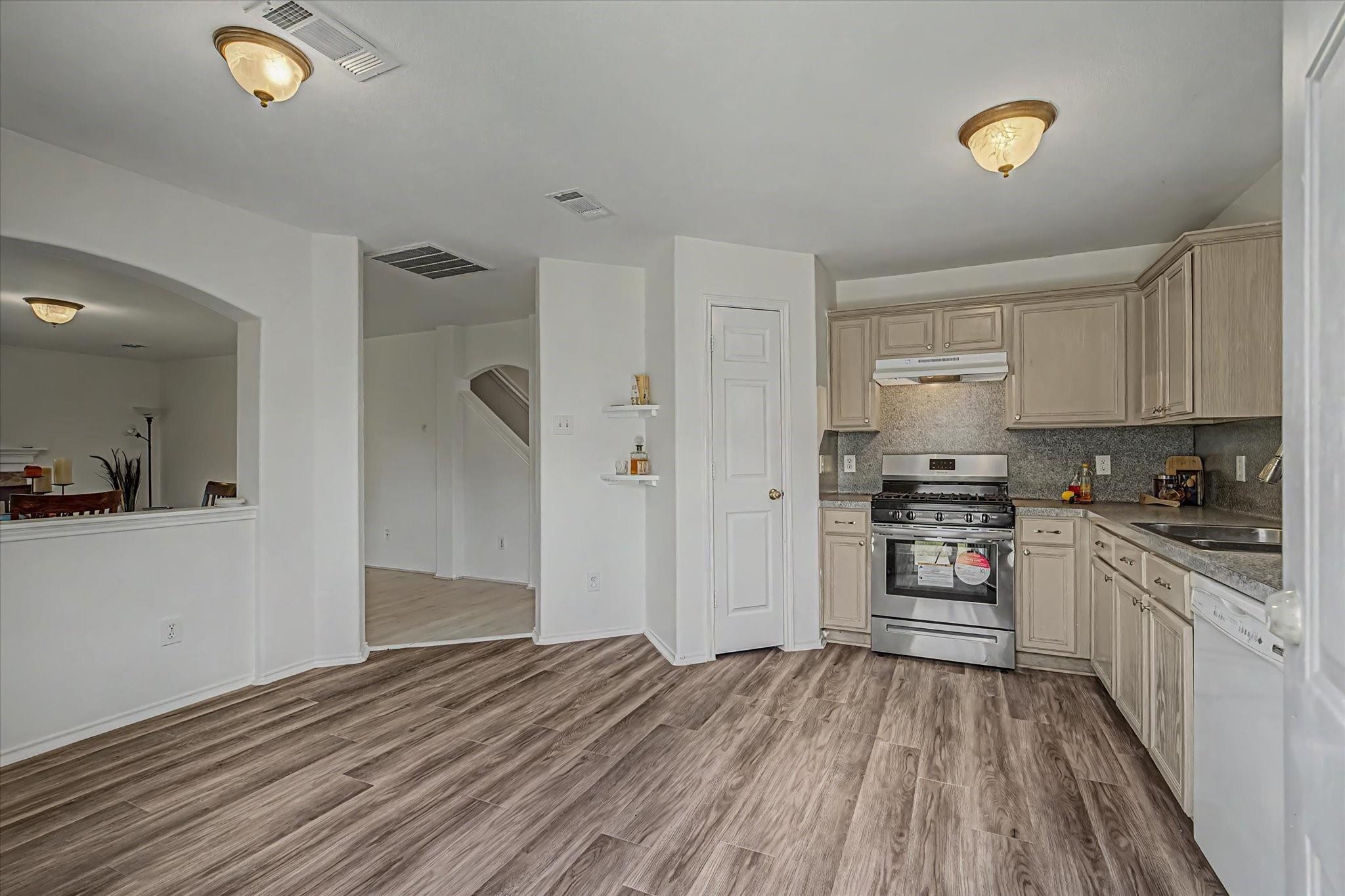 Open kitchen with light wood cabinets, stainless steel appliances, and wood-look floors.