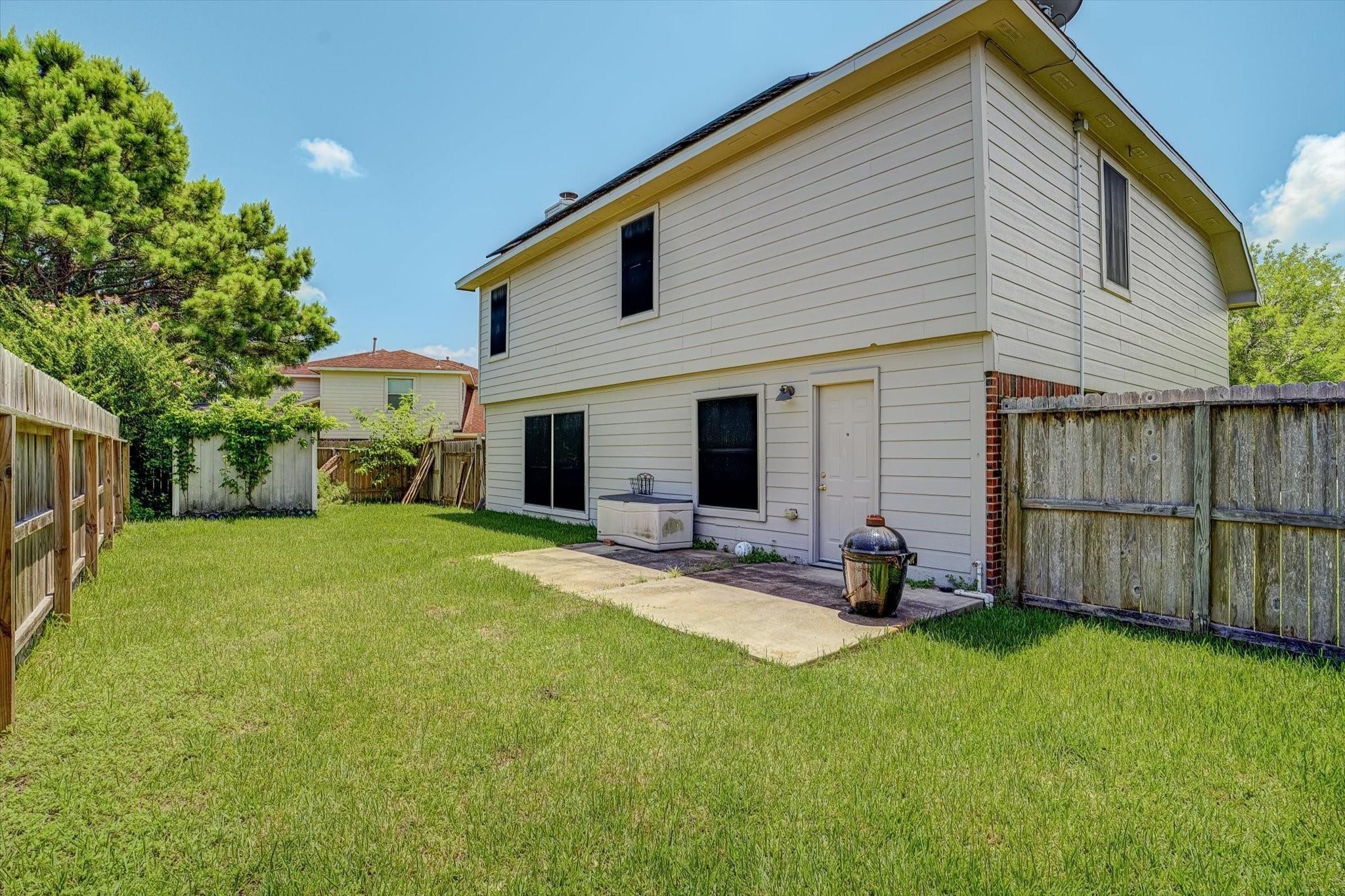 Two-story house behind a fenced grassy backyard, with a concrete patio and ceramic grill.
