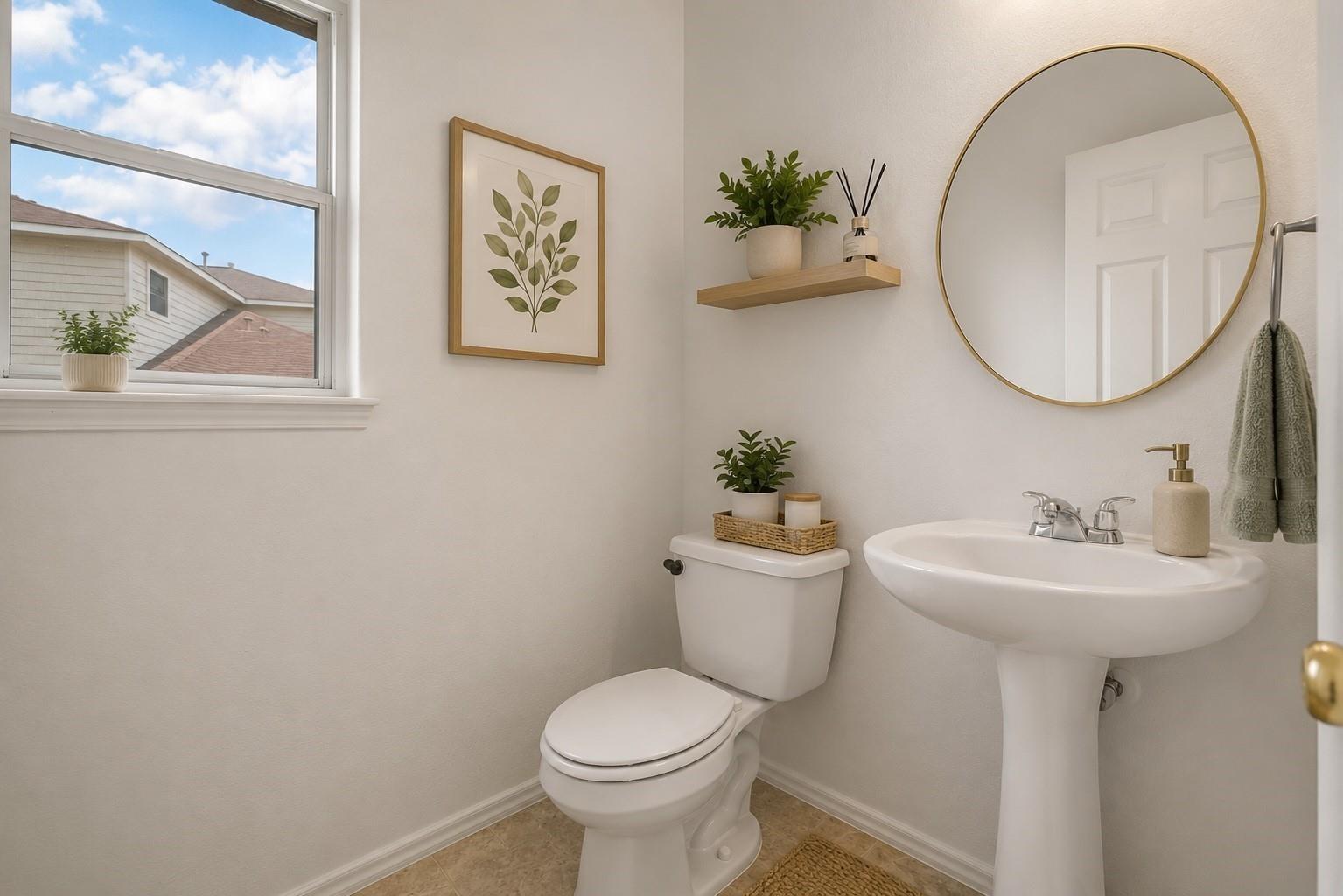 Staged half bathroom with a pedestal sink, toilet, round mirror, and window.