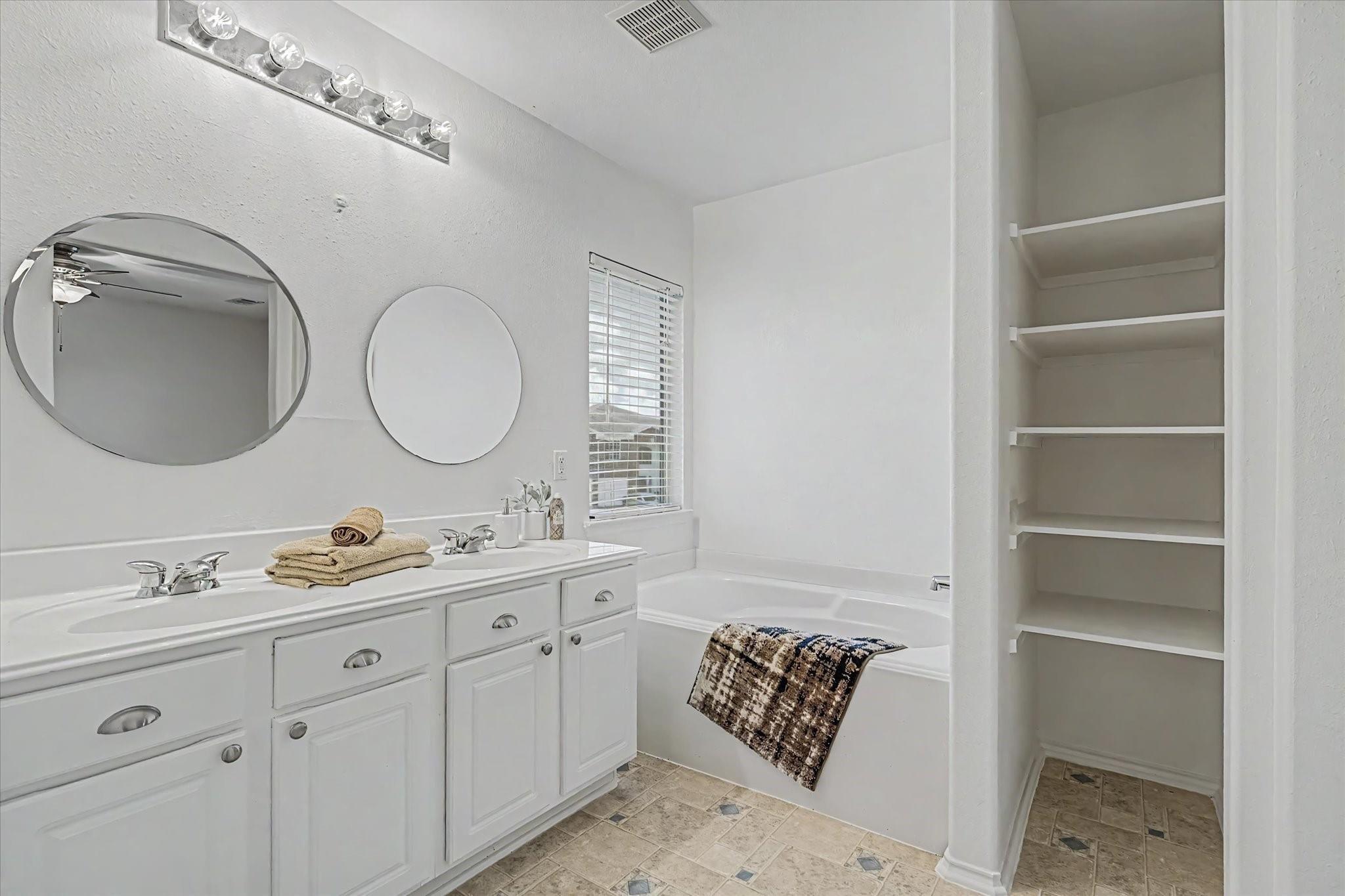 Bathroom with a white double vanity, round mirrors, bathtub, and built-in shelving nook.