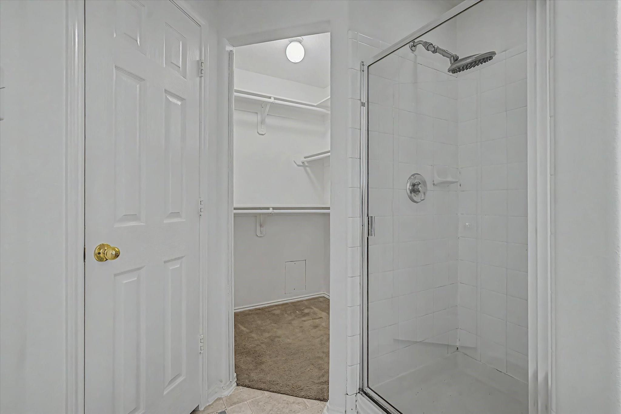 Bathroom with a glass shower beside an open walk-in closet with built-in shelves.
