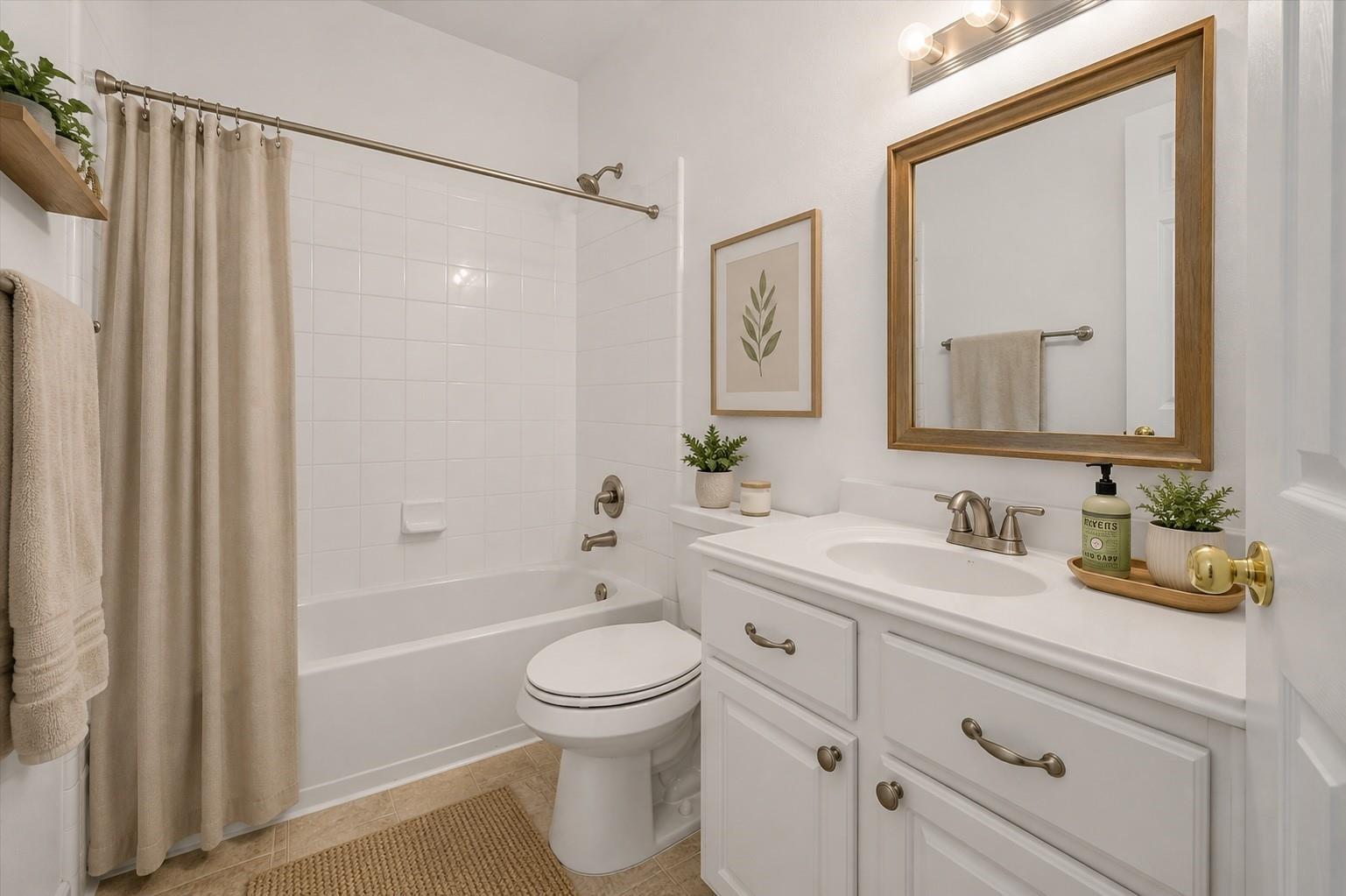Bathroom with a white tub, beige shower curtain, and white vanity beneath a wood-framed mirror.