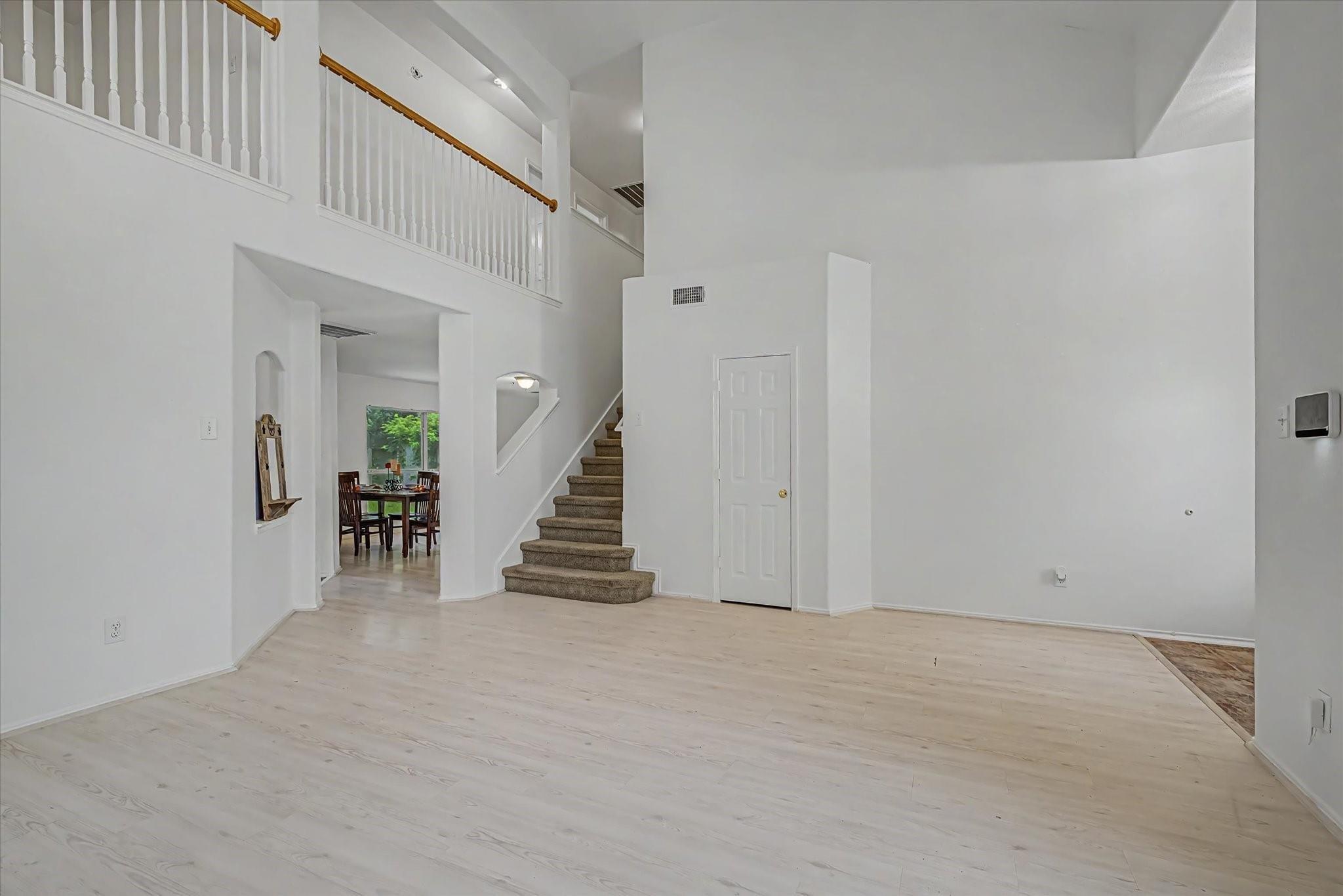 Two-story living room with pale wood floors, a carpeted staircase, and an upstairs balcony railing.