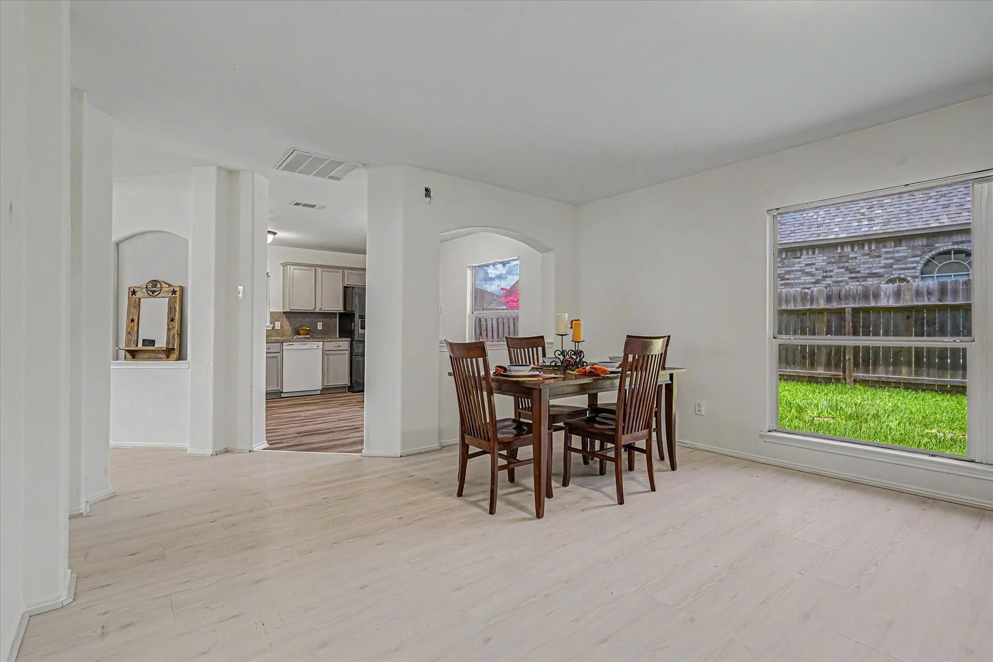 Dining area with a dark wood table, pale plank flooring, and a large window overlooking the fenced yard.