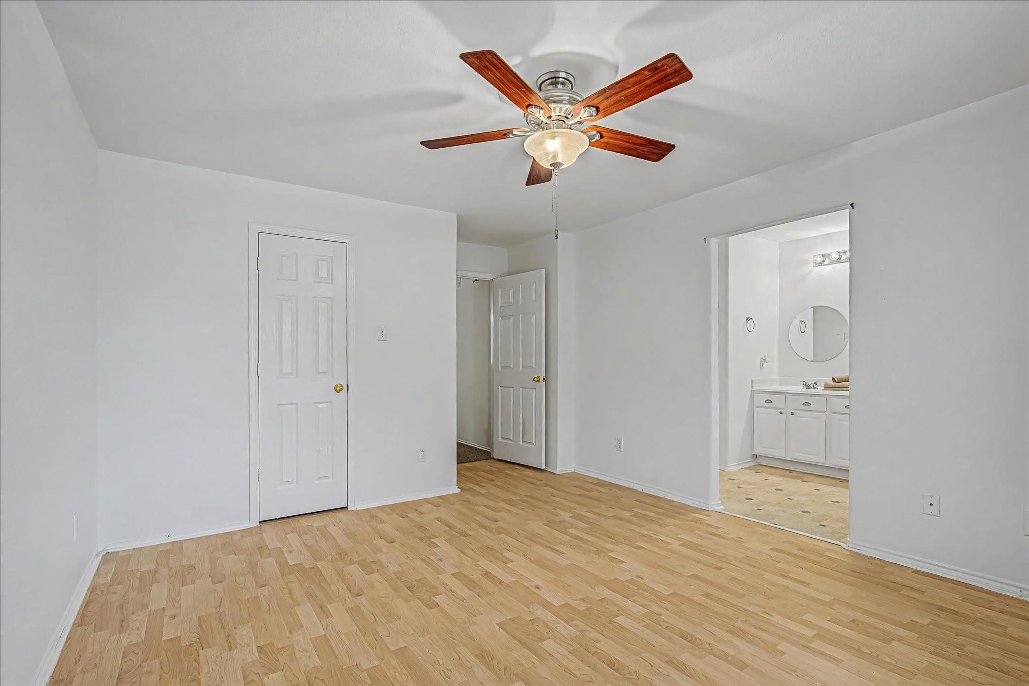Vacant bedroom with light wood floors, a ceiling fan, and an adjoining bathroom.