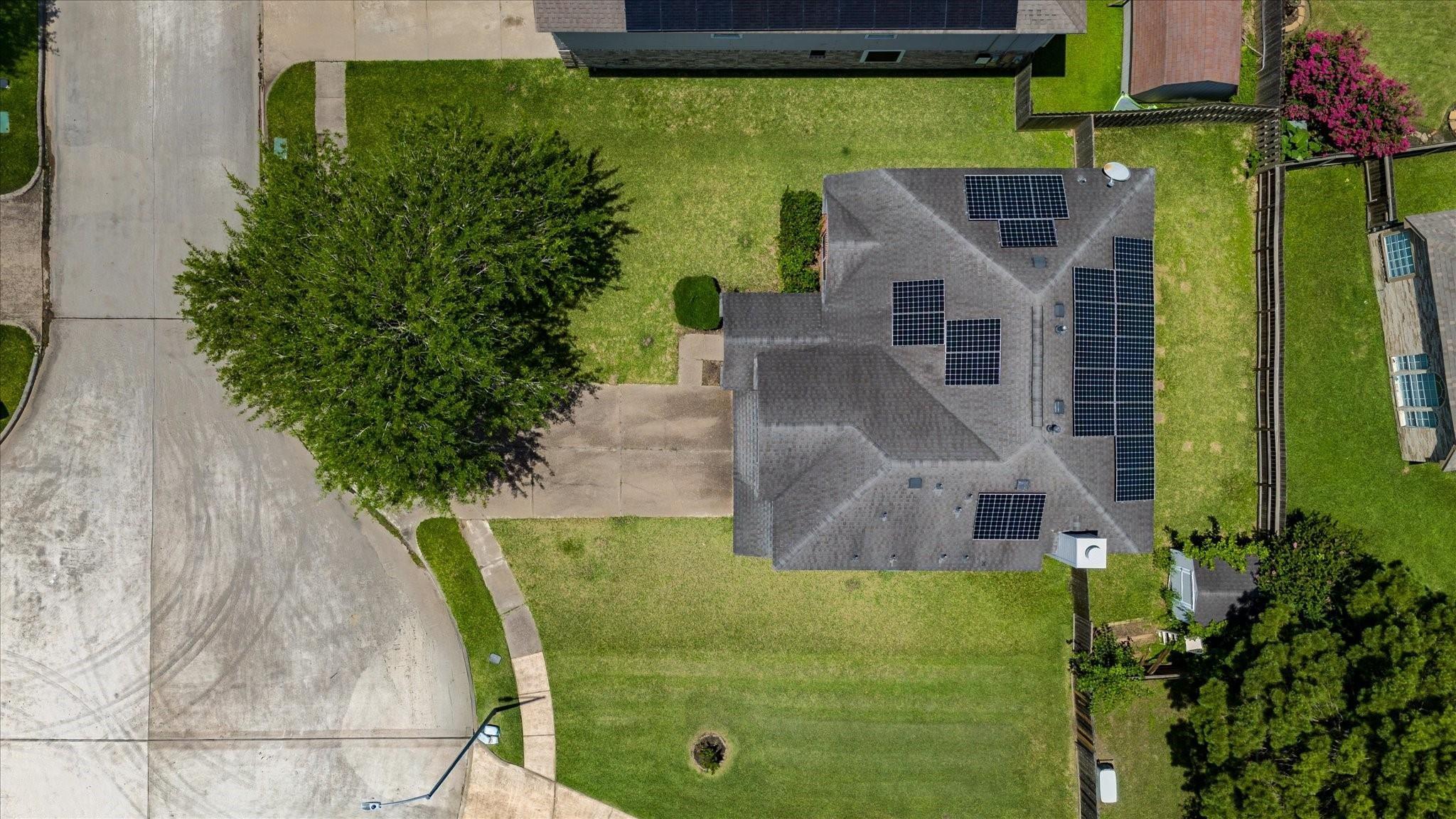 Aerial view of a house with multiple solar panels on its roof and a wide green lawn.