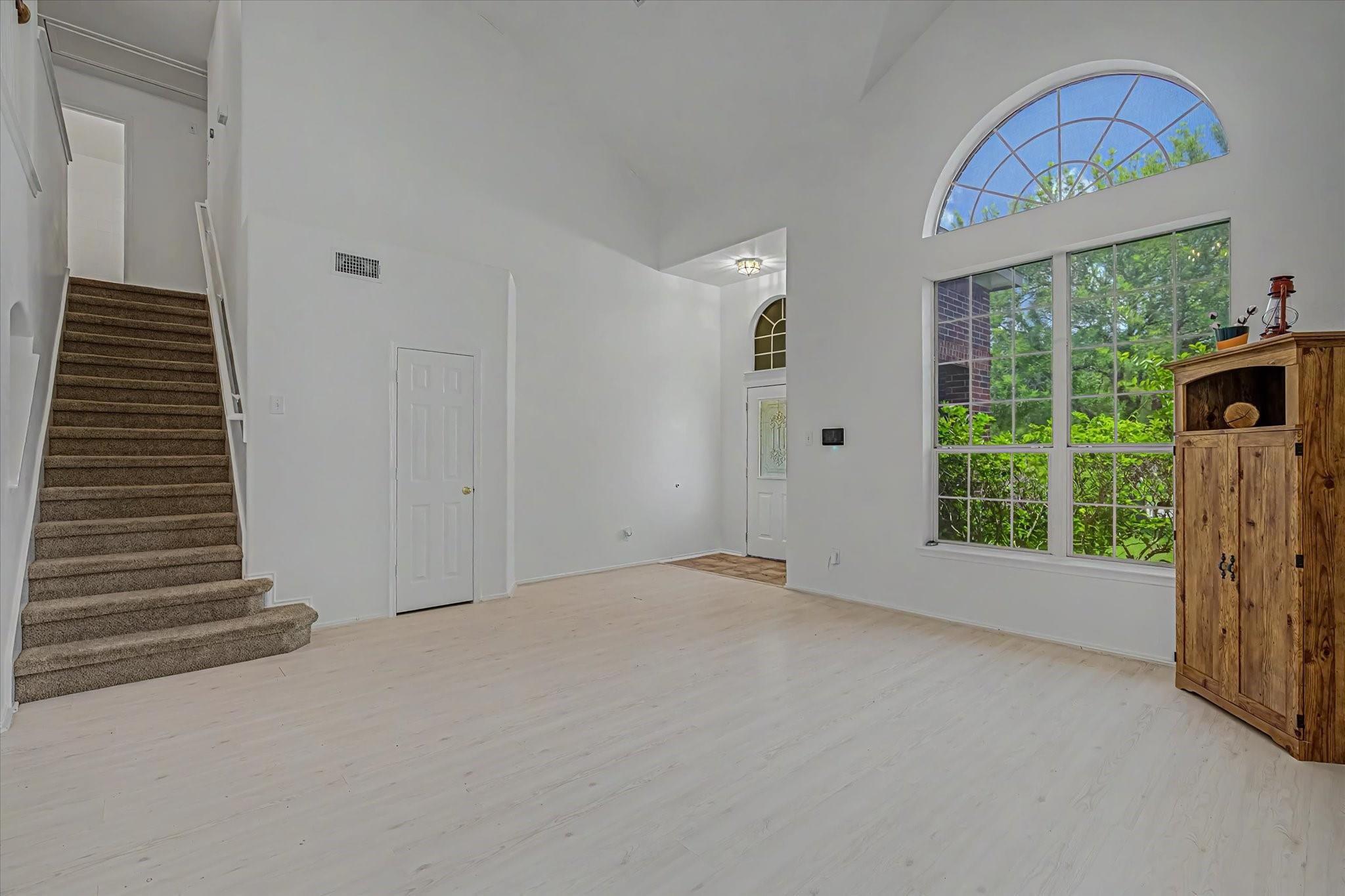 Living room with vaulted ceiling, carpeted staircase, and large arched windows.