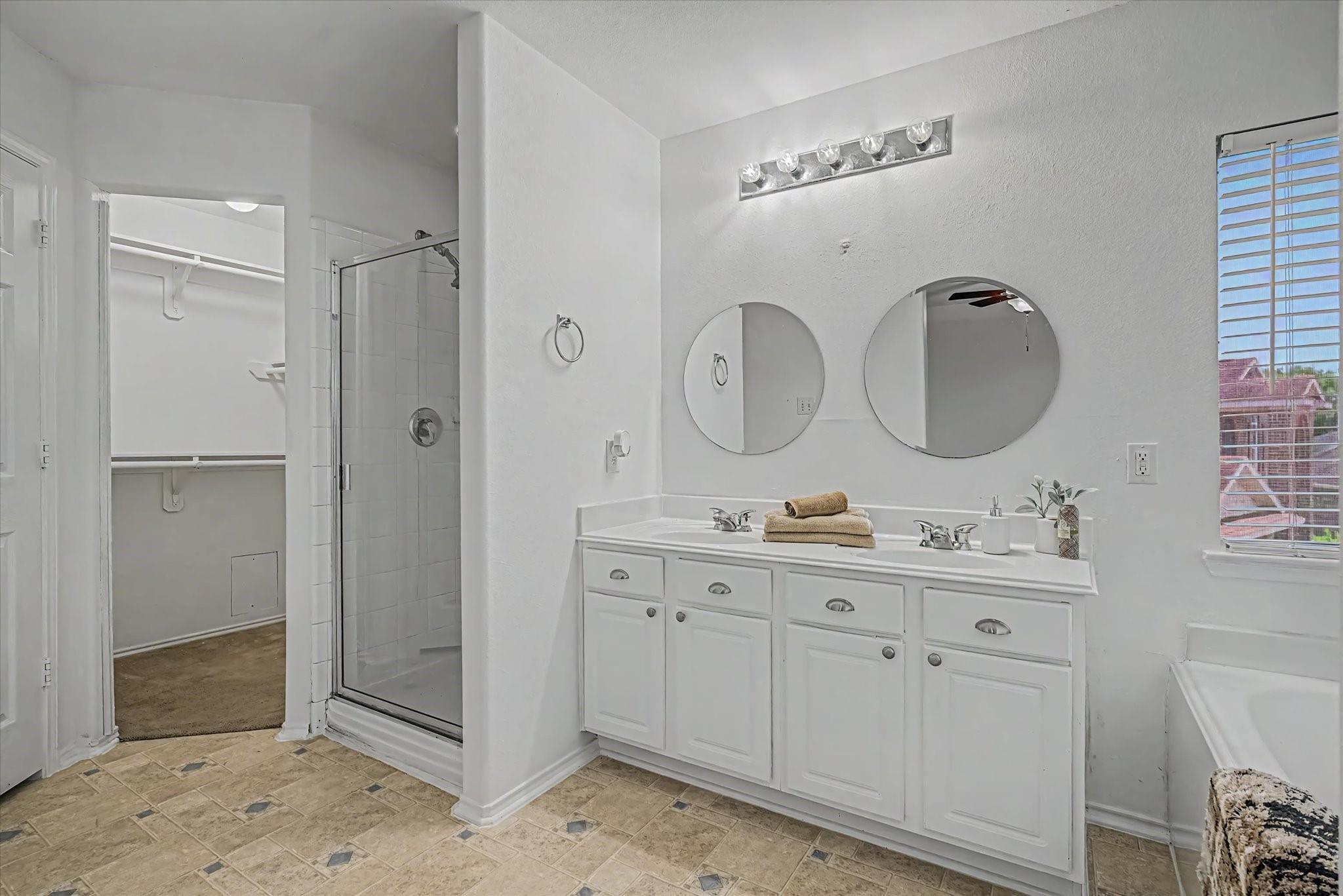 Bathroom with a double-sink vanity, two round mirrors, and glass-enclosed shower.