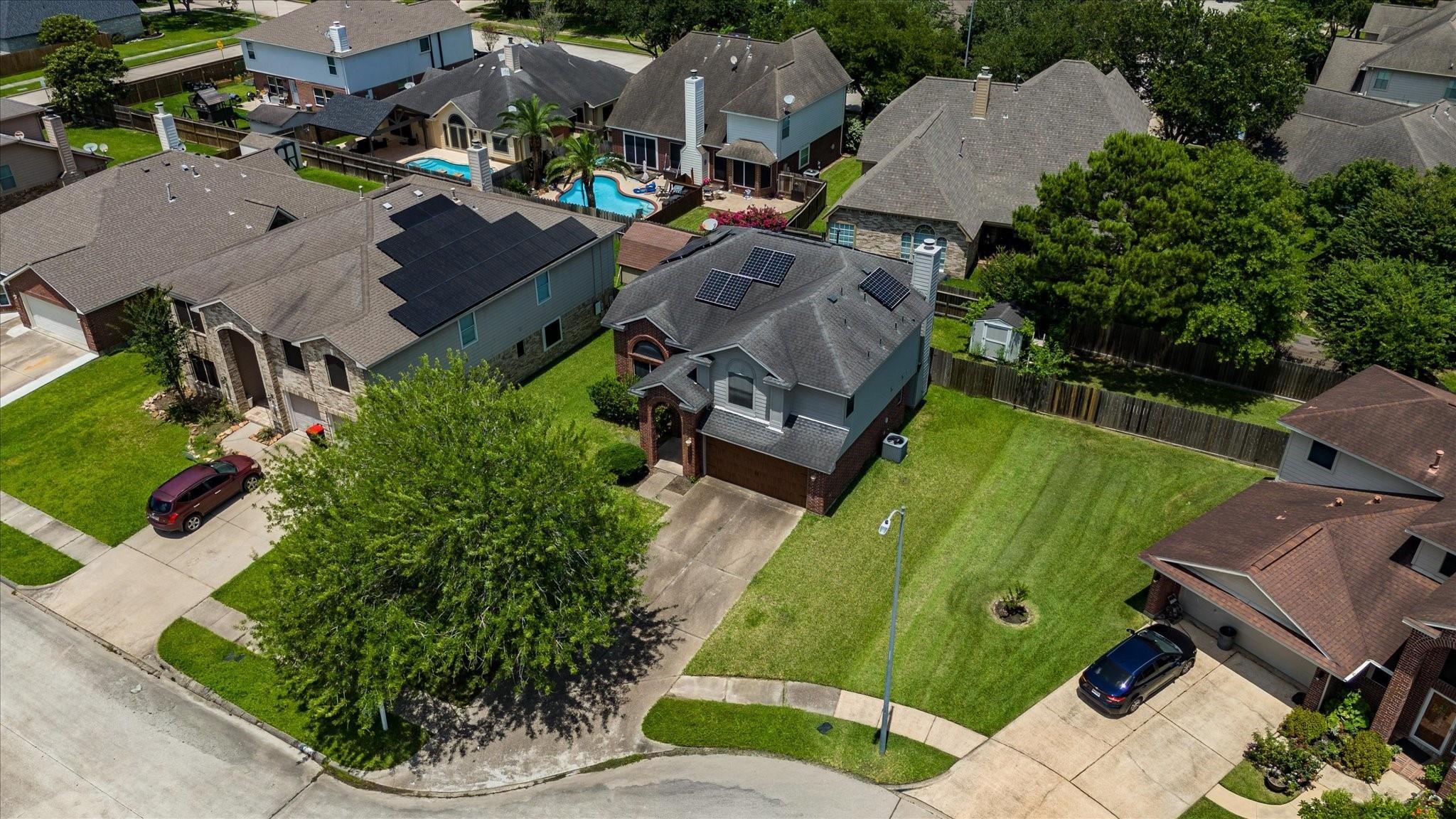 Aerial view of a two-story house with solar panels and a fenced backyard.