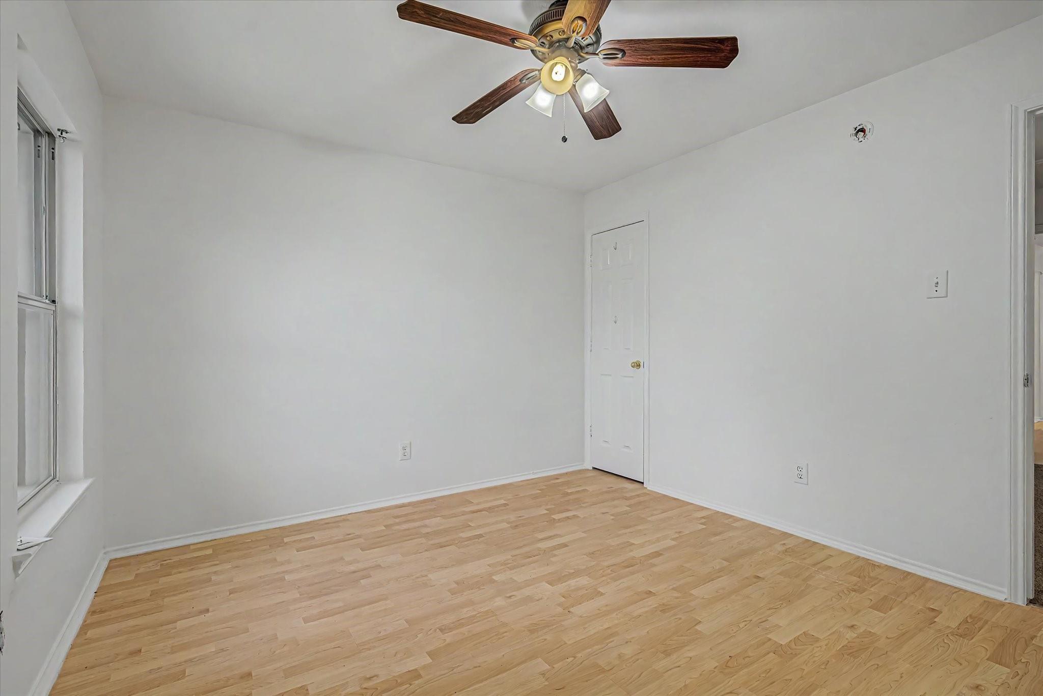 Empty bedroom with light hardwood floors and a wooden-blade ceiling fan.