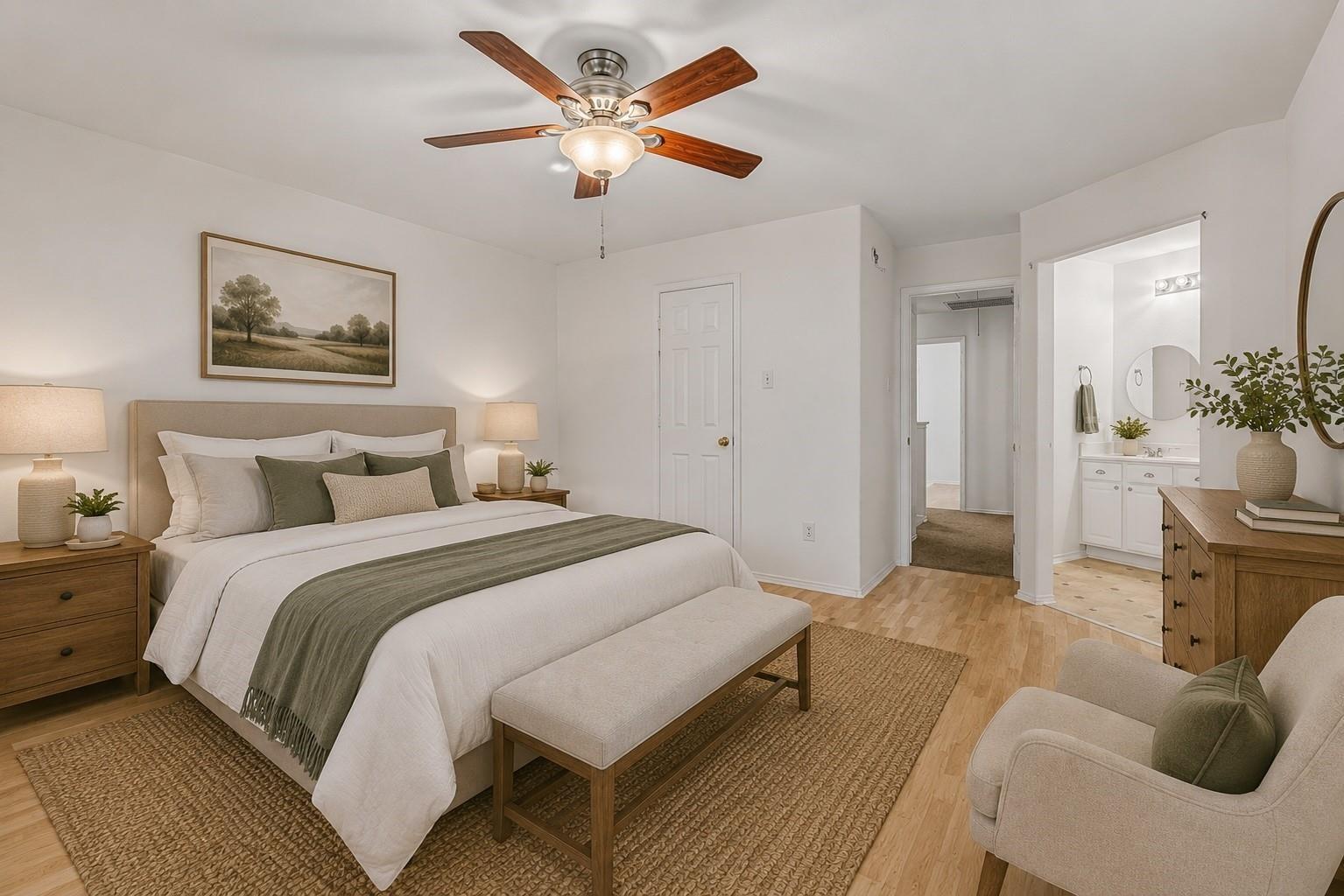 Staged bedroom with a white bed, sage-green throw, wood furnishings, and an adjoining bathroom.