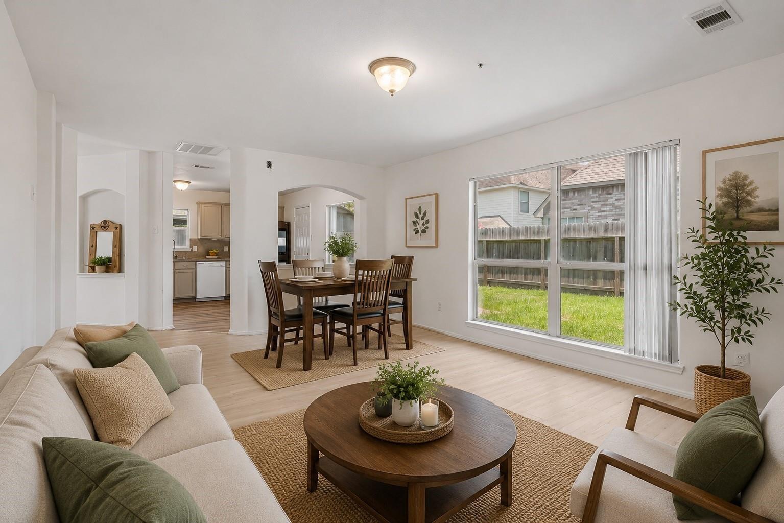 Living and dining room with neutral sofas, a dark wood dining set, and a large backyard-facing window.