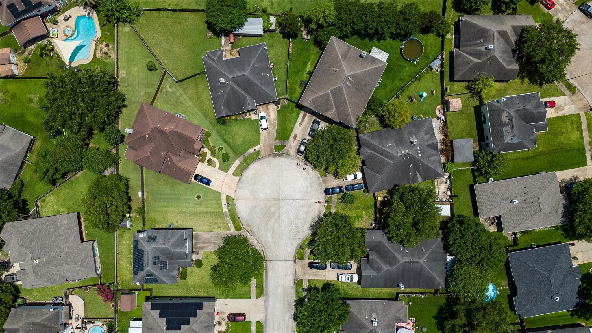 Aerial view of homes and green yards around a tree-lined cul-de-sac.