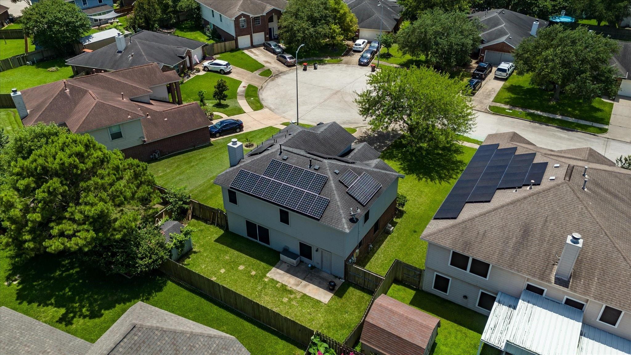 Aerial view of a home with rooftop solar panels beside a quiet cul-de-sac.