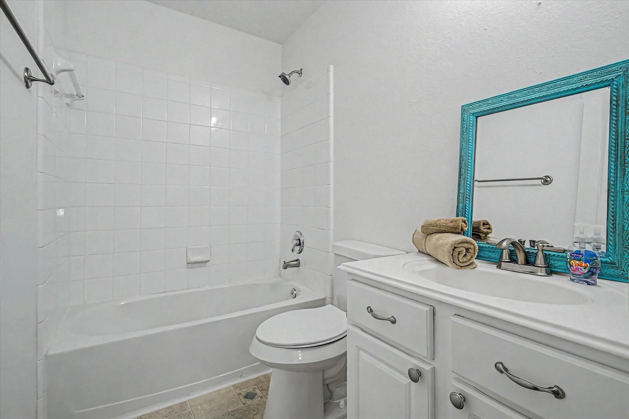 Bathroom with a white tiled tub and shower, vanity, and ornate turquoise-framed mirror.