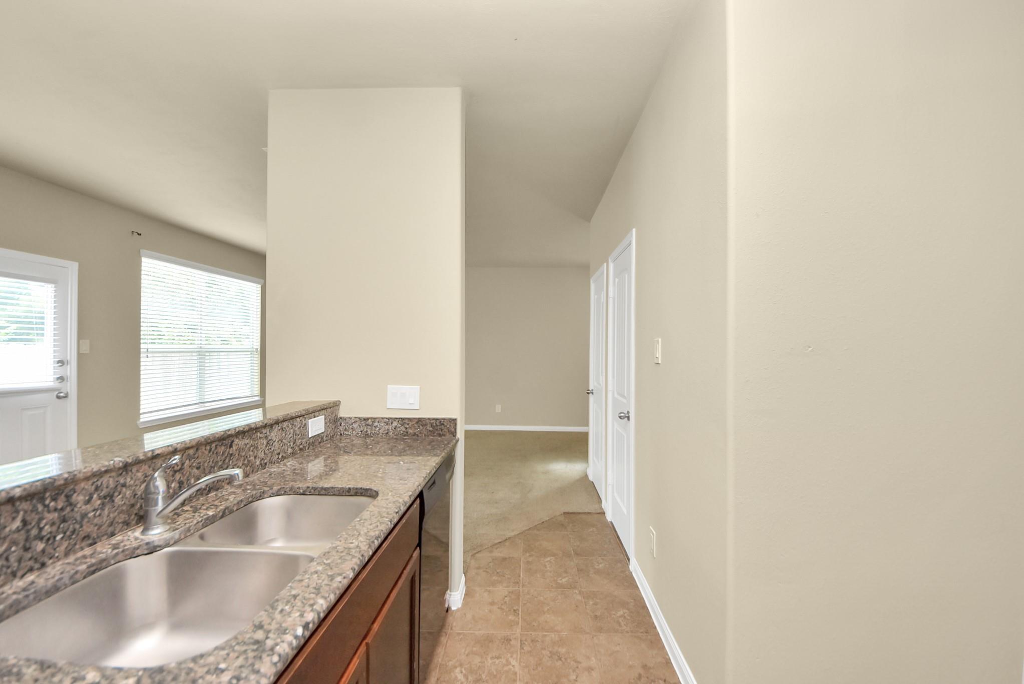Kitchen with a double-basin sink, granite counters, and a tiled floor leading to a hallway.