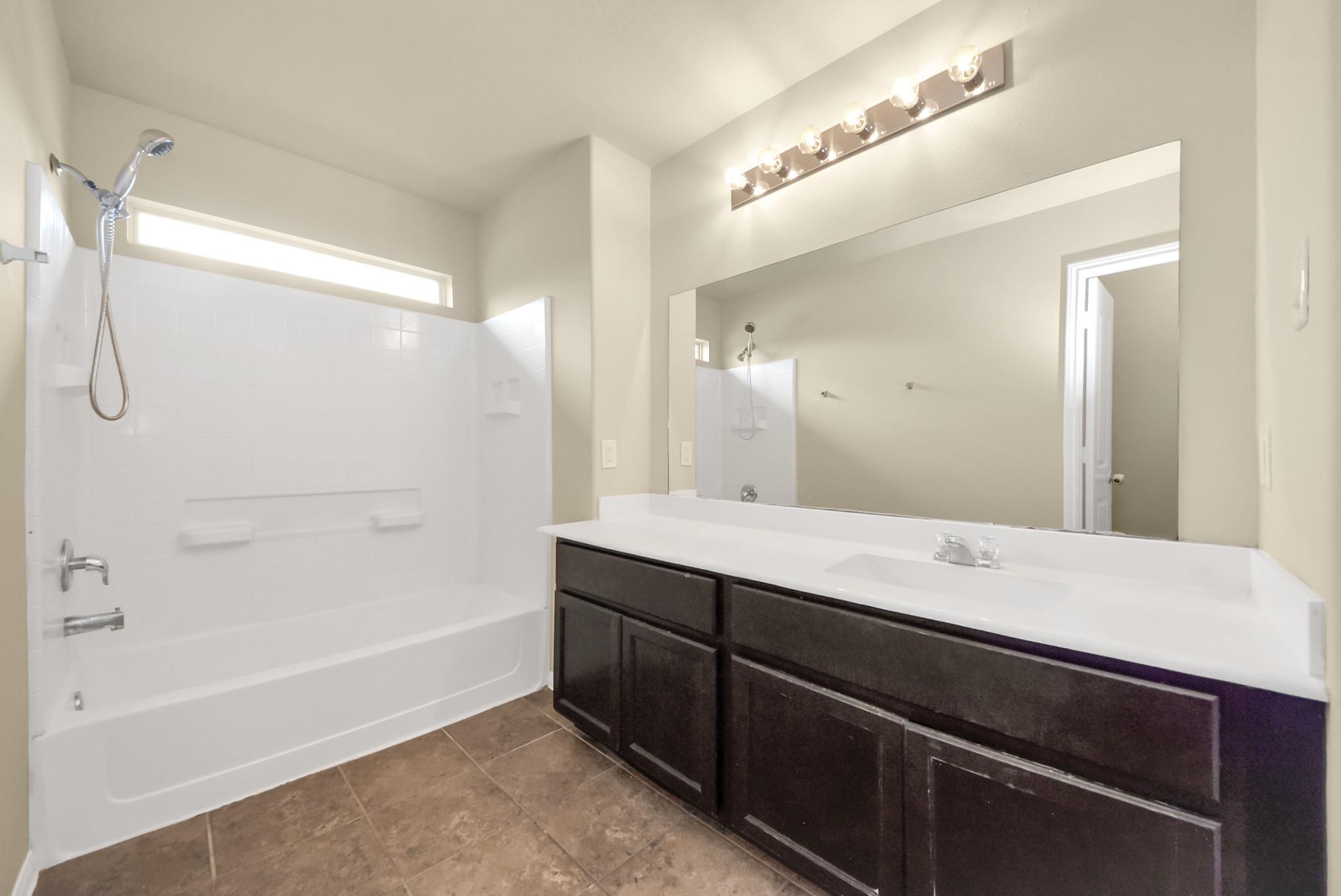 Bathroom with a white tub and shower beside a dark wood vanity and large mirror.
