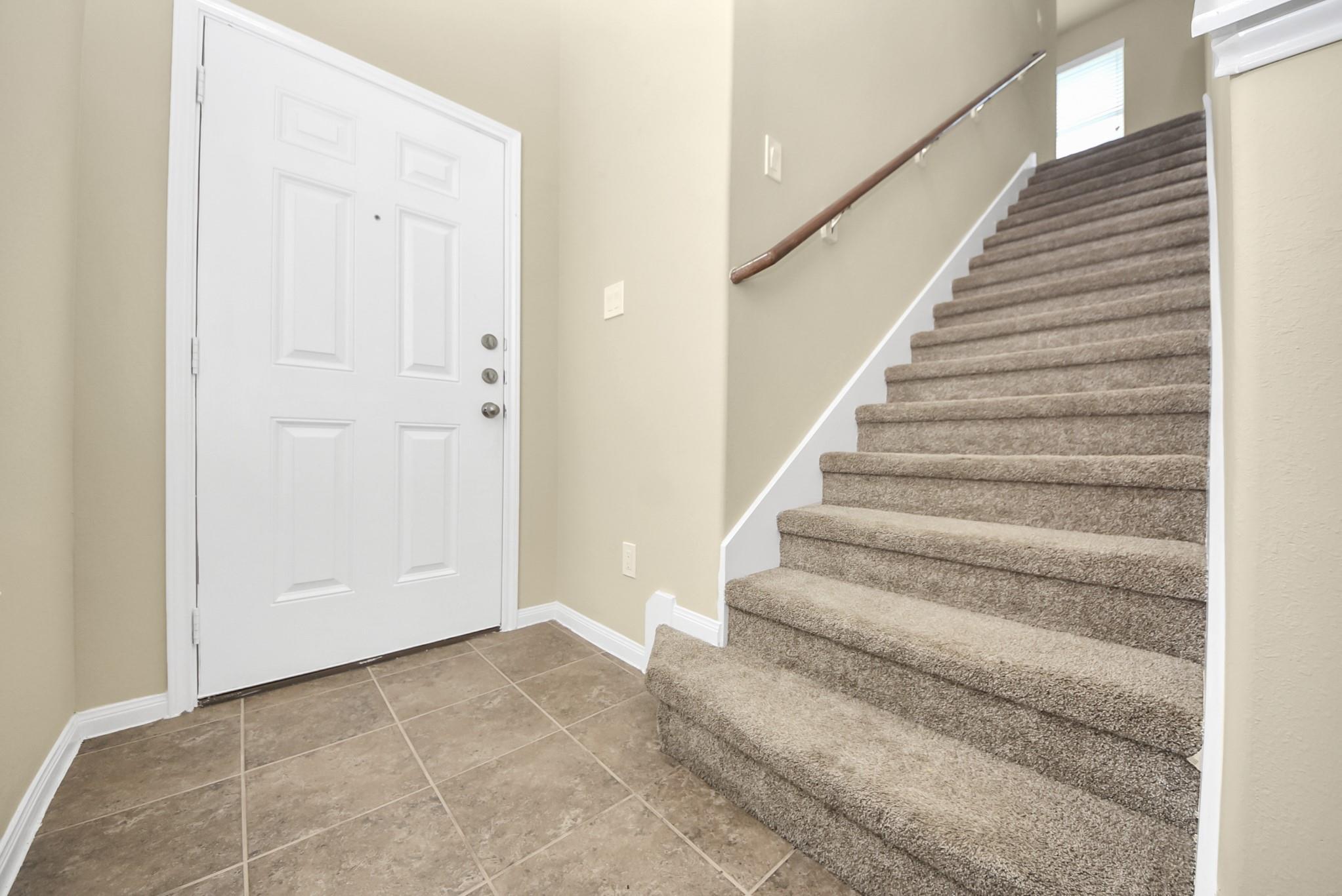 Entry foyer with a white front door, tiled floor, and carpeted staircase.