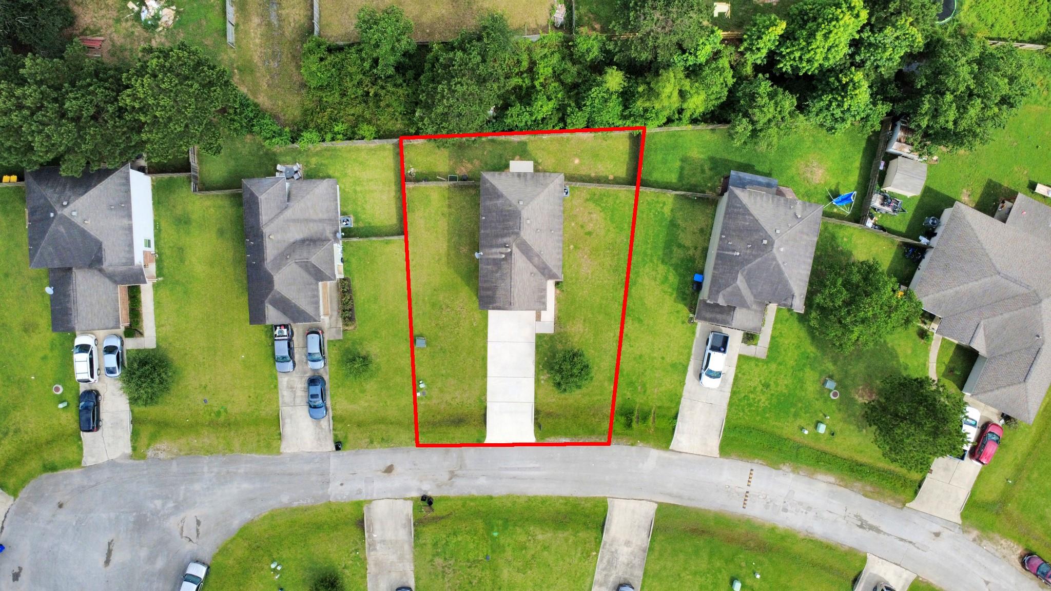 Aerial view of a house and lot outlined in red, with a long driveway and fenced backyard.