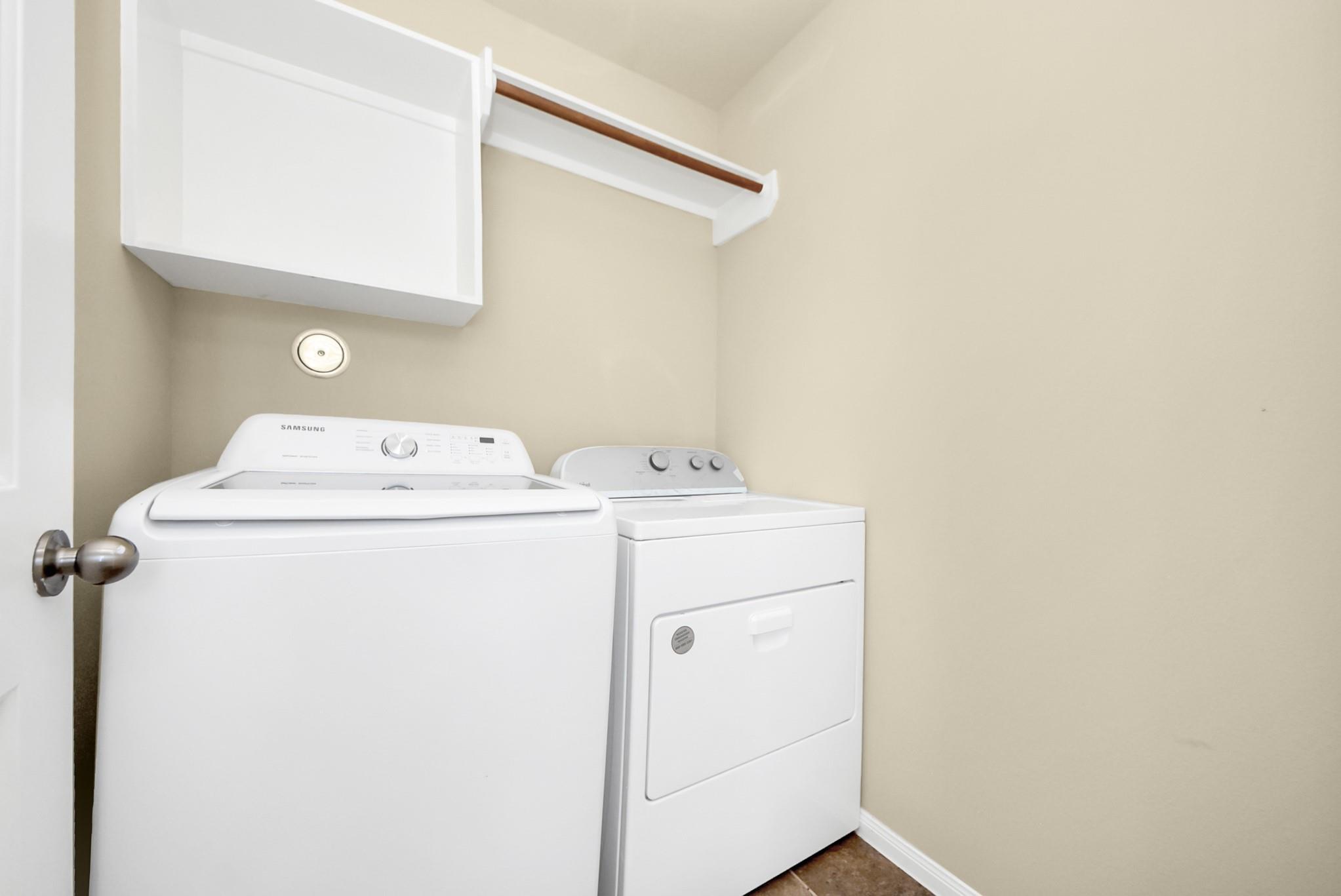 Laundry room with a white washer and dryer beneath an overhead shelf and hanging rod.