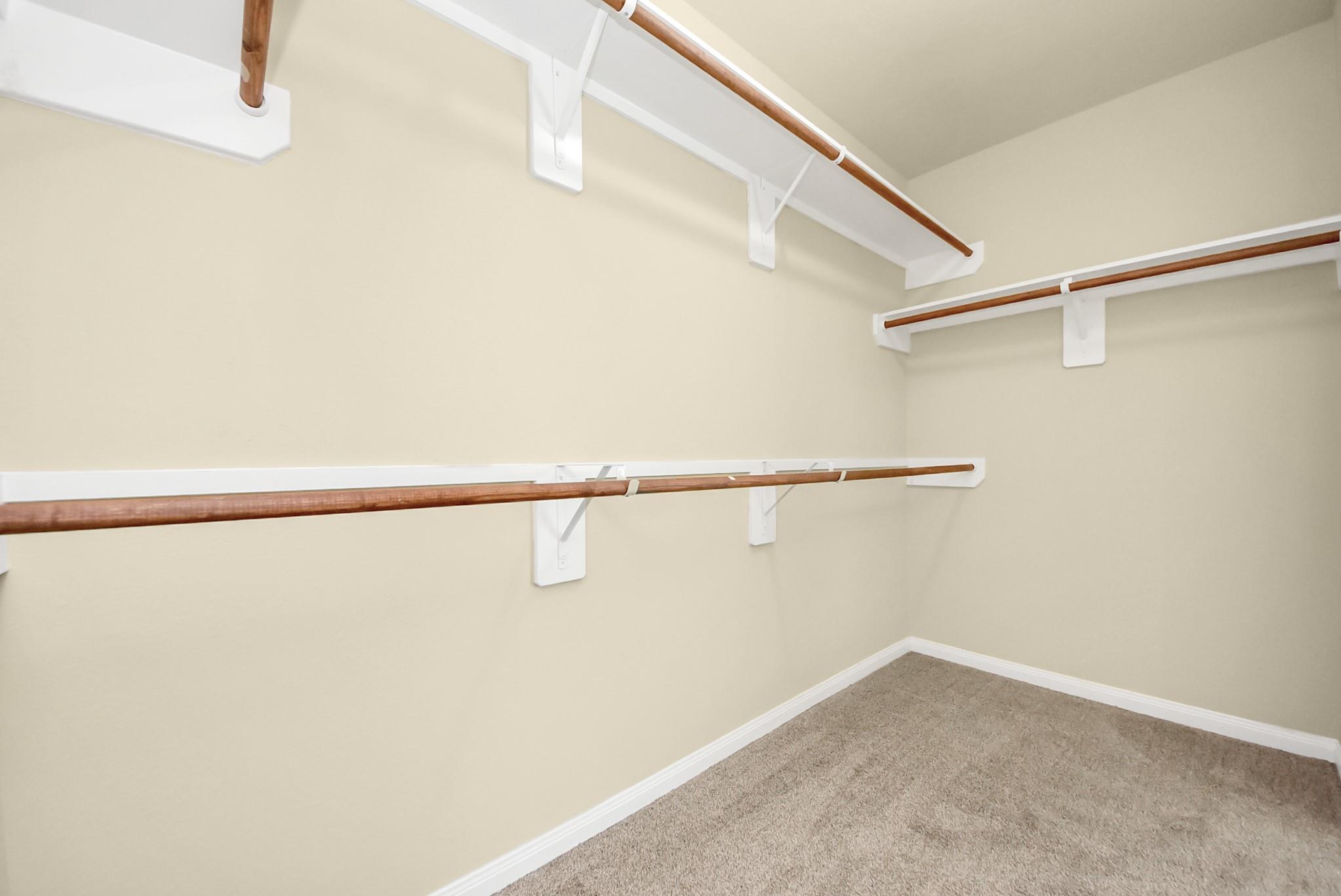 Empty walk-in closet with wooden clothes rods and tan carpet.