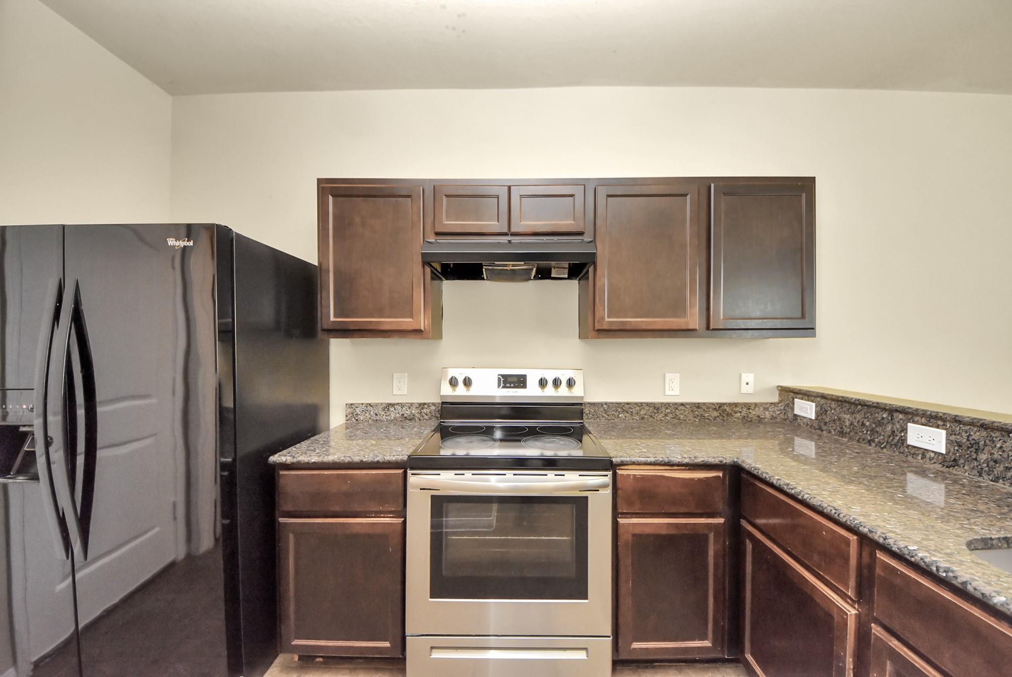 Kitchen with dark wood cabinets, stone countertops, and stainless steel range.