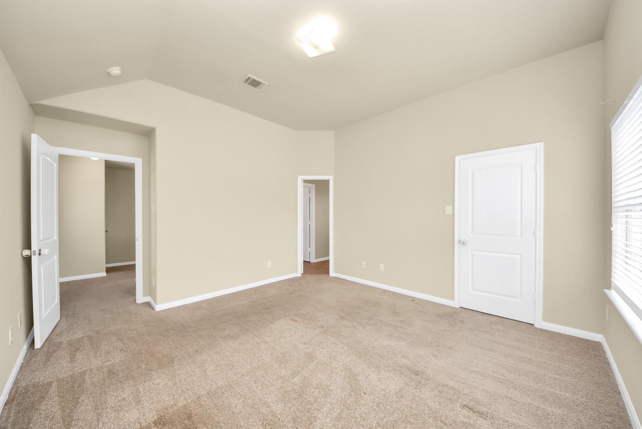 Empty bedroom with taupe carpet, a vaulted ceiling, and a window with blinds.