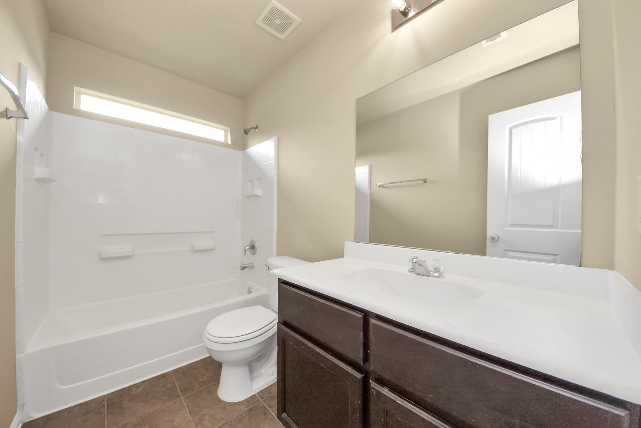 Bathroom with a white tub and shower, dark wood vanity, and high horizontal window.