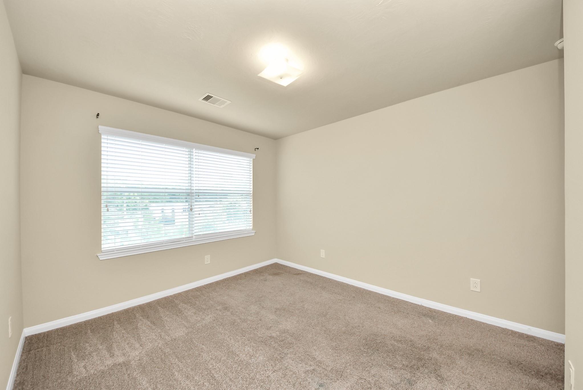 Empty carpeted room with beige walls and a wide window with white blinds.