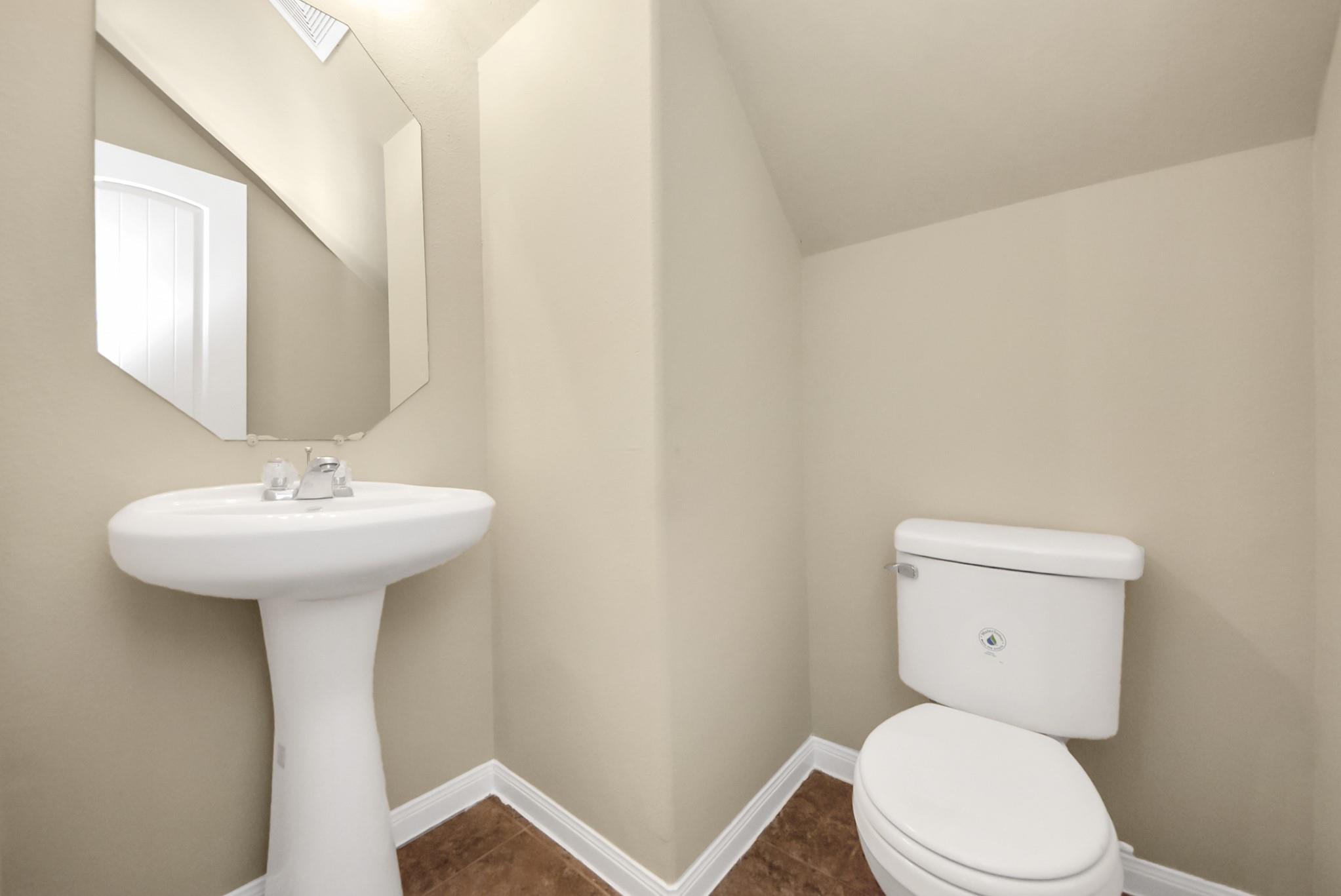 Bathroom with a pedestal sink, toilet, large mirror, and brown tile floor.