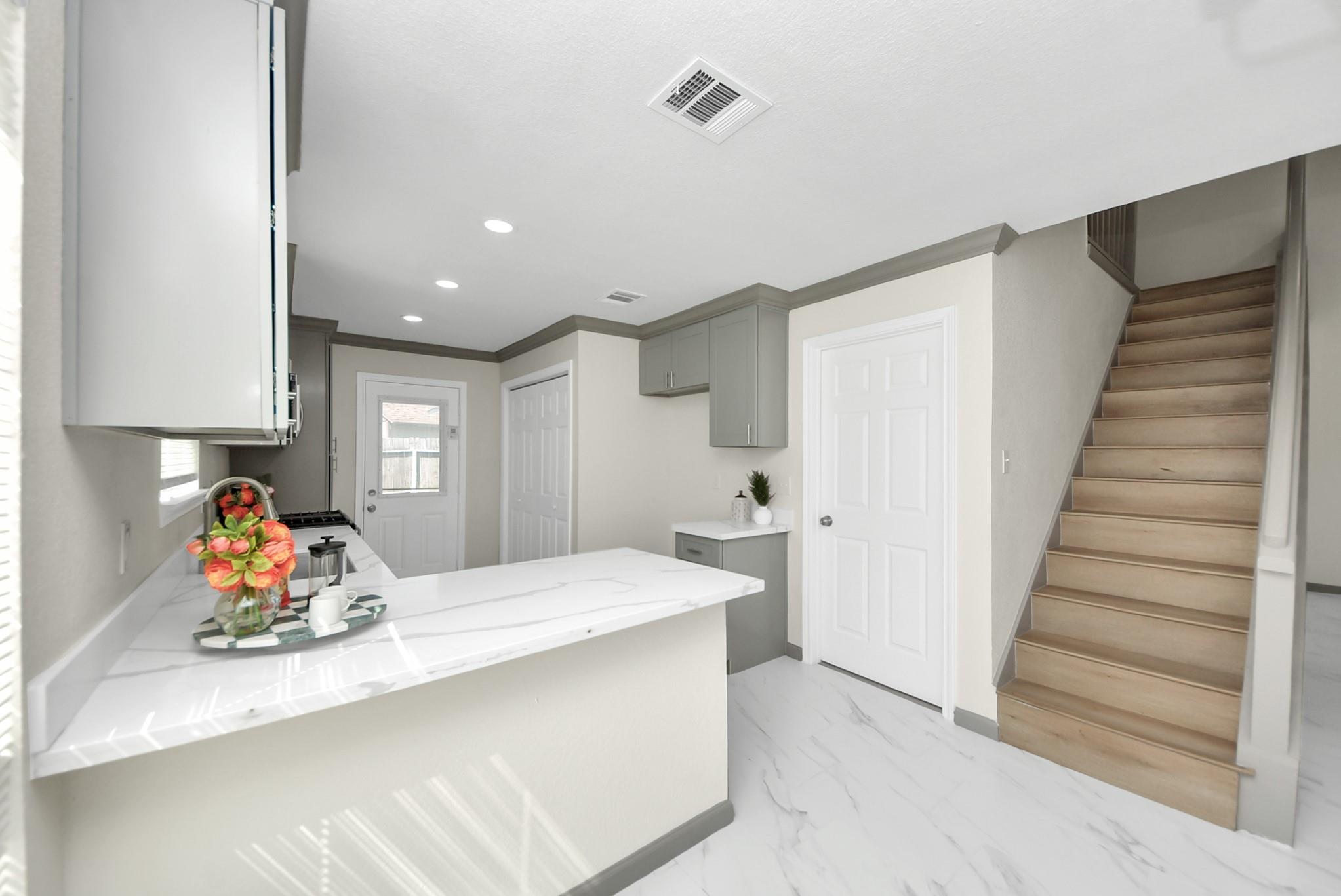 Kitchen with white counters and gray cabinets beside a staircase.