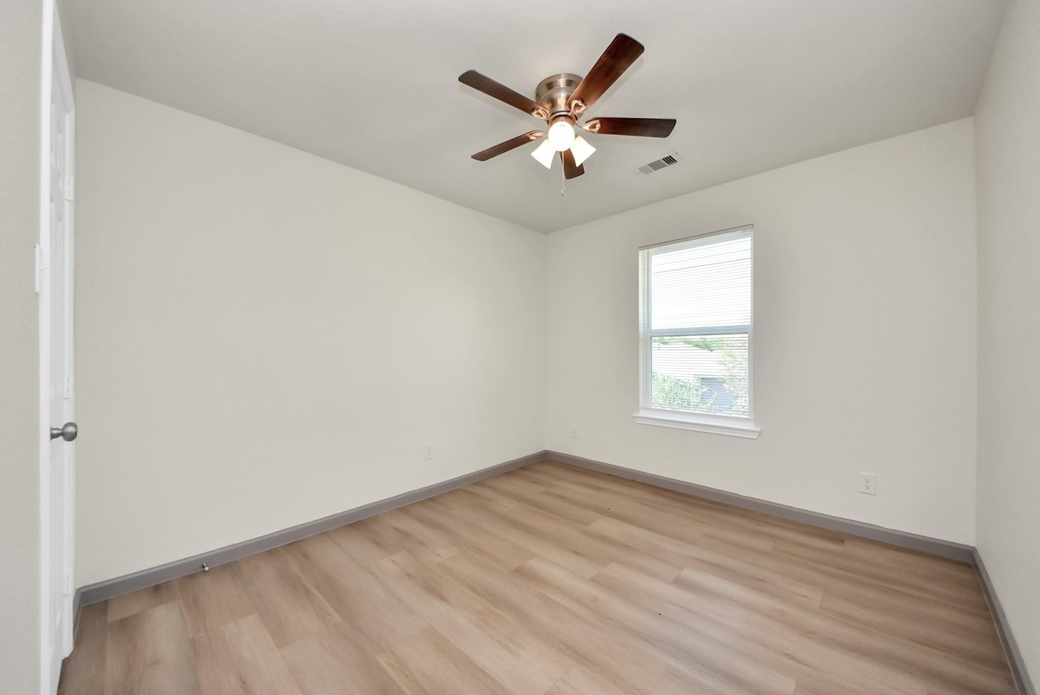 Empty bedroom with light wood flooring, a ceiling fan, and a window with blinds.