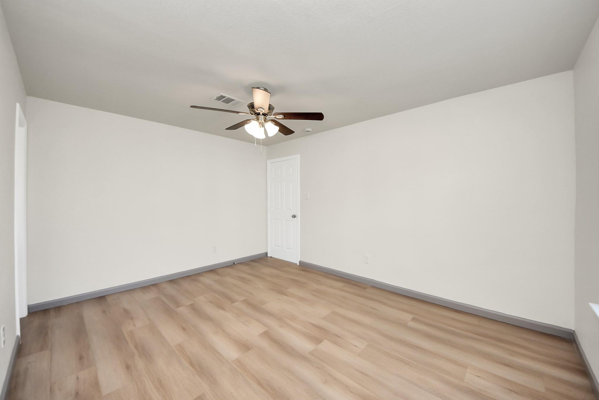 Empty room with light wood-look flooring and a ceiling fan with lights.