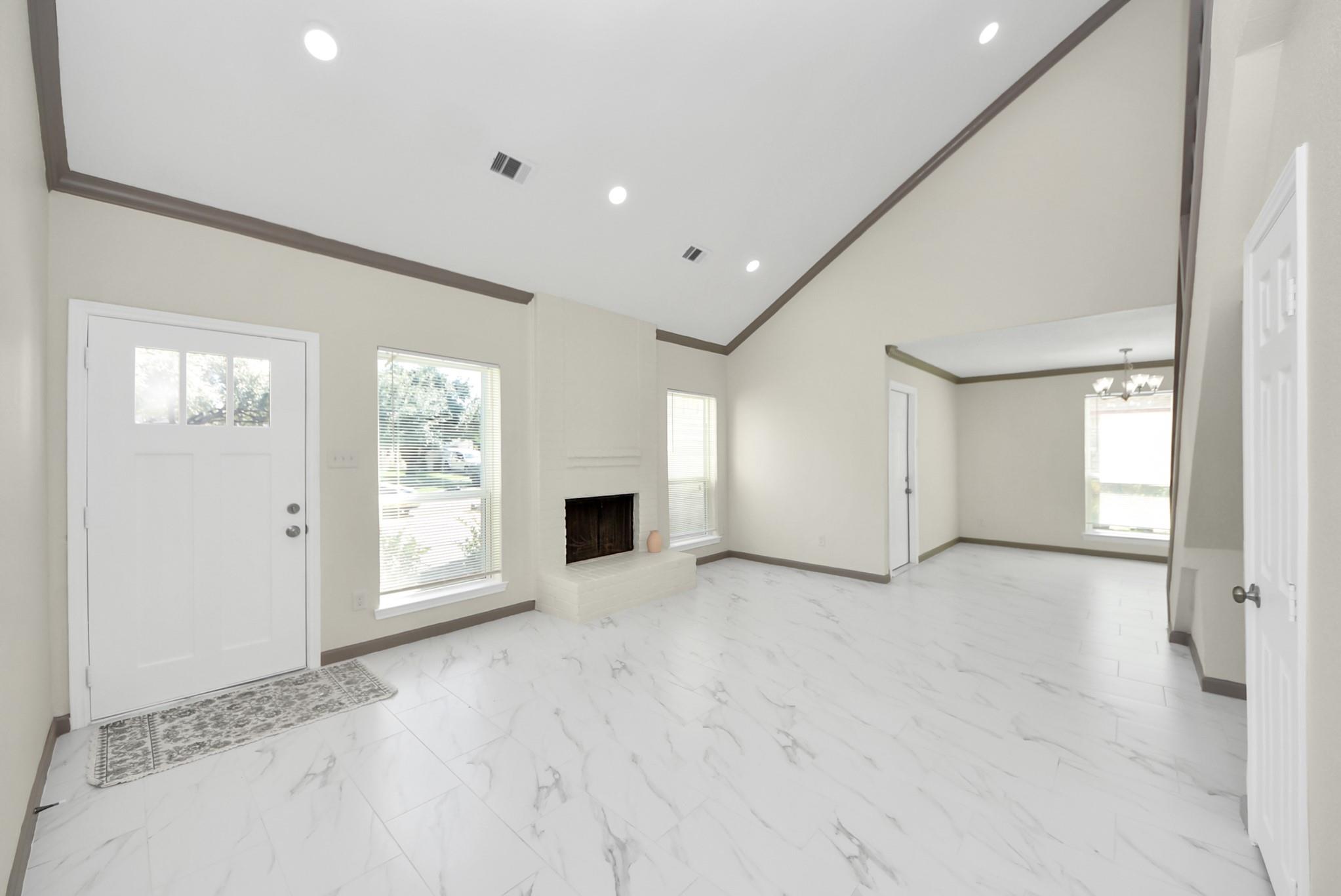 Living room with vaulted ceiling, marble-look tile floors, and a fireplace beside the front door.