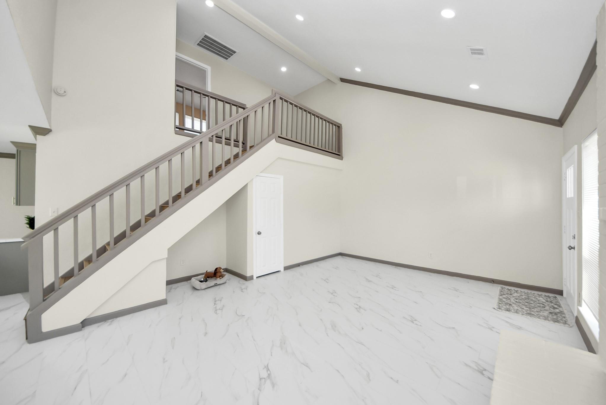 Empty living room with marble-look floors, a gray-railed staircase, and a high tray ceiling.