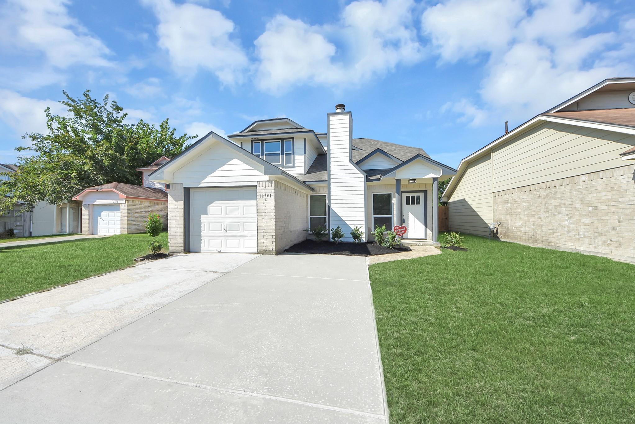 Light-colored home with an attached garage, broad driveway, and green front lawn.