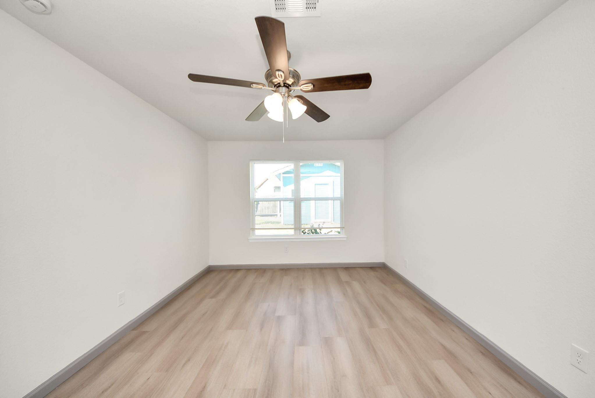Vacant bedroom with light wood-look flooring, a ceiling fan, and a window with blinds.