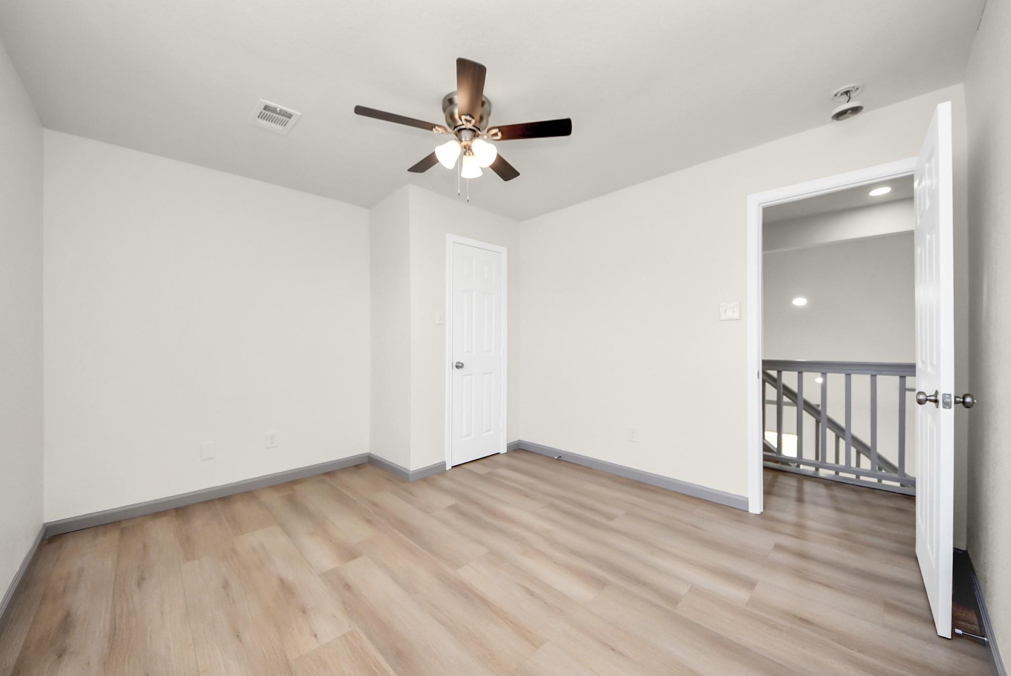 Empty room with wood-look flooring, ceiling fan, and doorway to an upstairs landing.