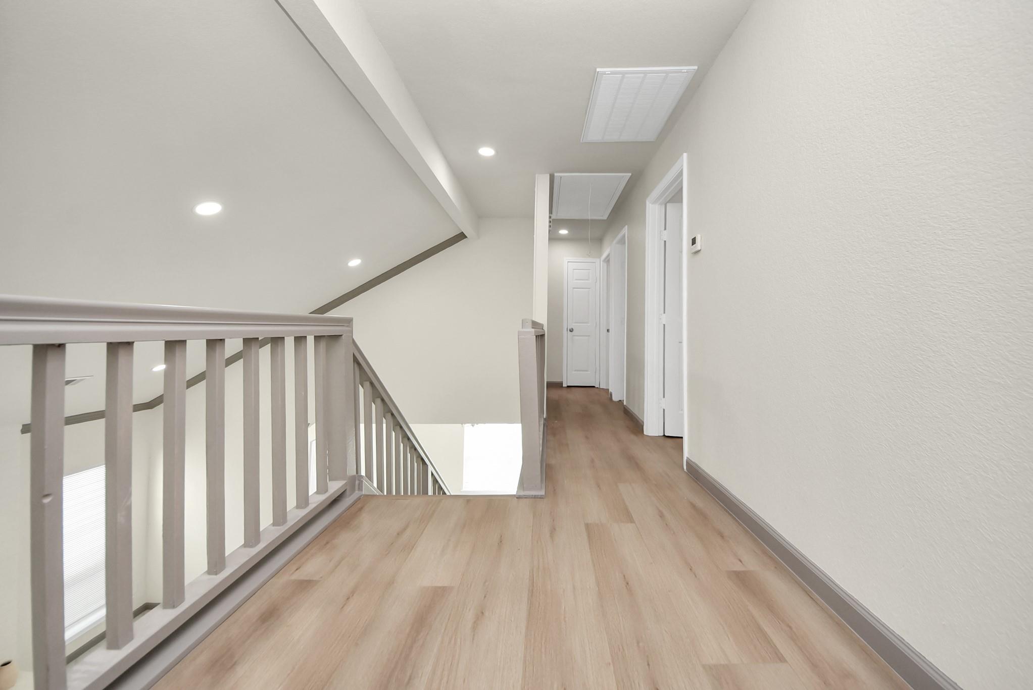 Upstairs landing with light wood-look flooring, white railing, and hallway doors.