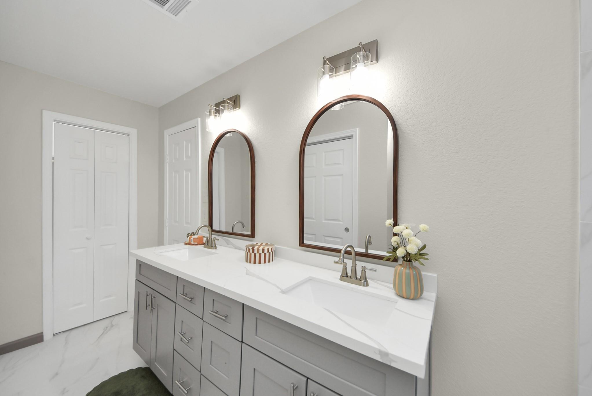 Bathroom double vanity with gray cabinetry, marble-look counter, and two arched wood-framed mirrors.