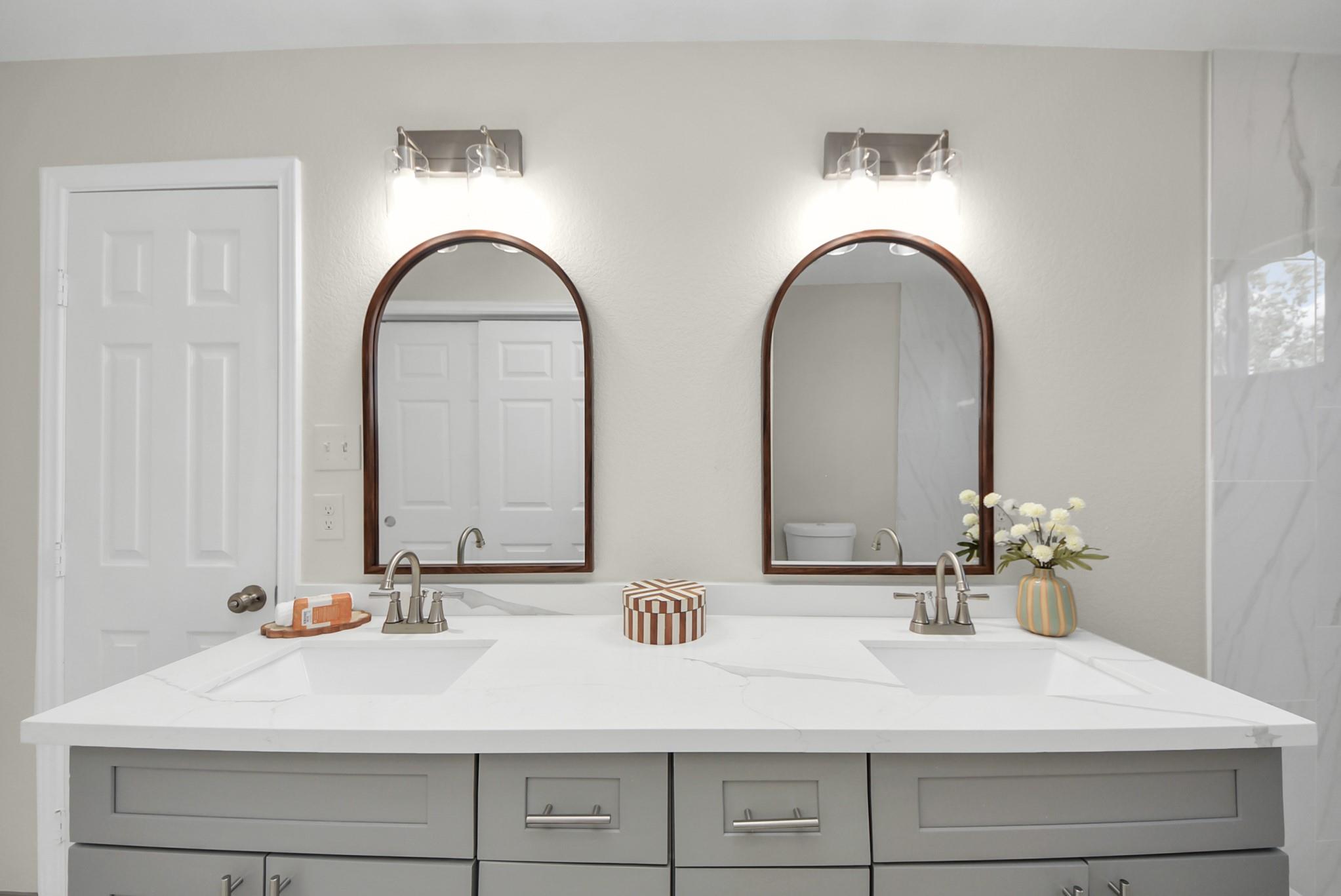 Bathroom vanity with two sinks, a white veined countertop, and matching arched mirrors.