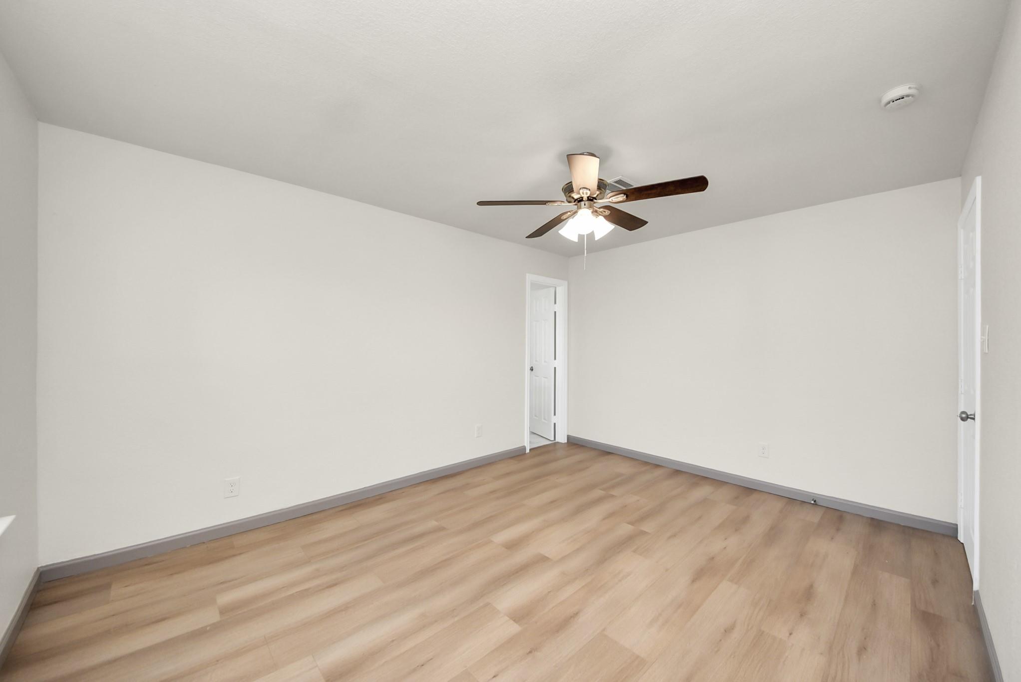 Empty room with light wood-look flooring and a ceiling fan with lights.