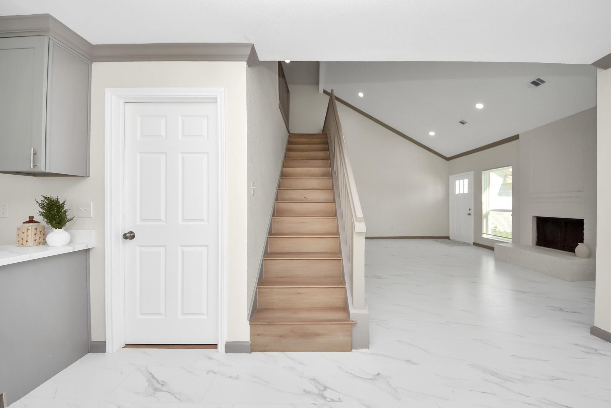 Entry and living area with a wood staircase, marble-look tile floors, and a fireplace.
