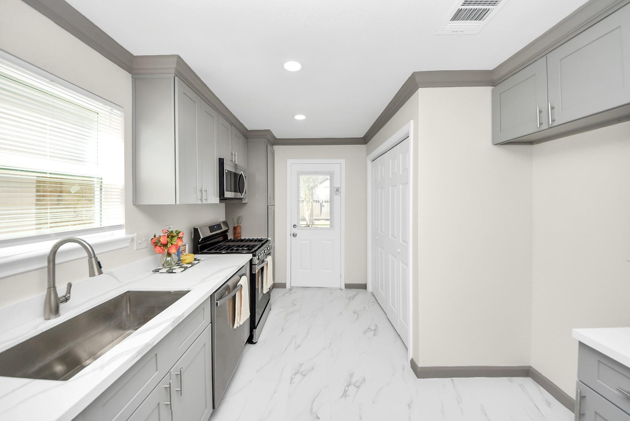 Kitchen with gray cabinets, white counters, stainless appliances, and marble-look flooring.