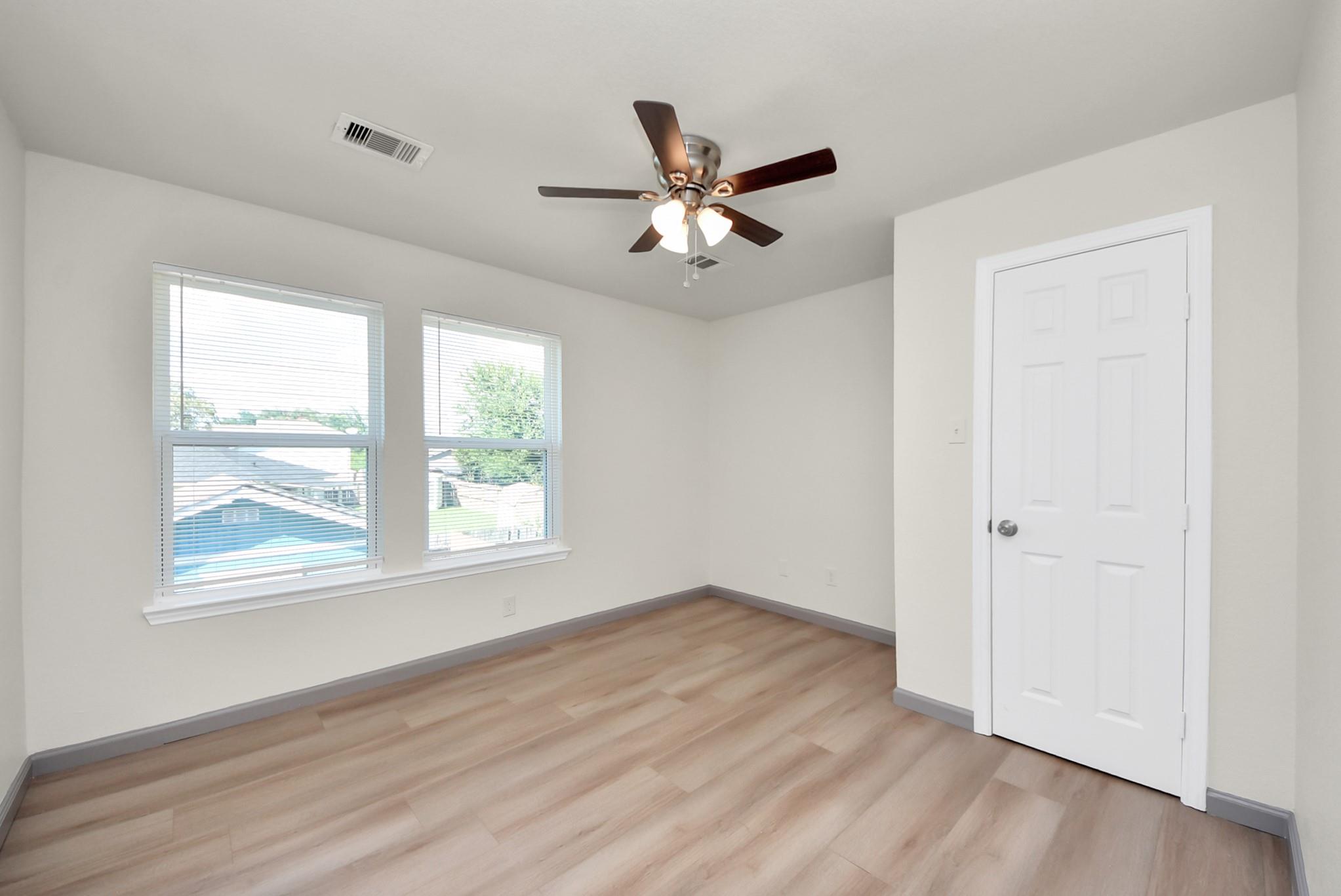 Vacant room with light wood-look flooring, two blinded windows, and a ceiling fan with lights.