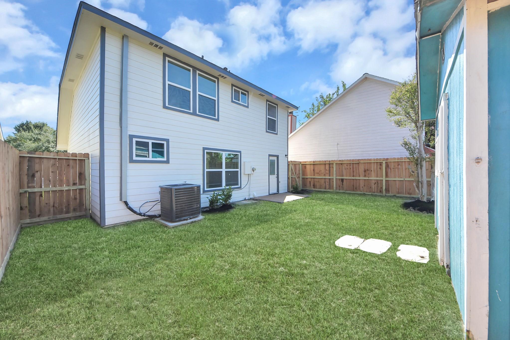 Two-story white house with blue-gray trim and a fenced grassy backyard with stepping stones.