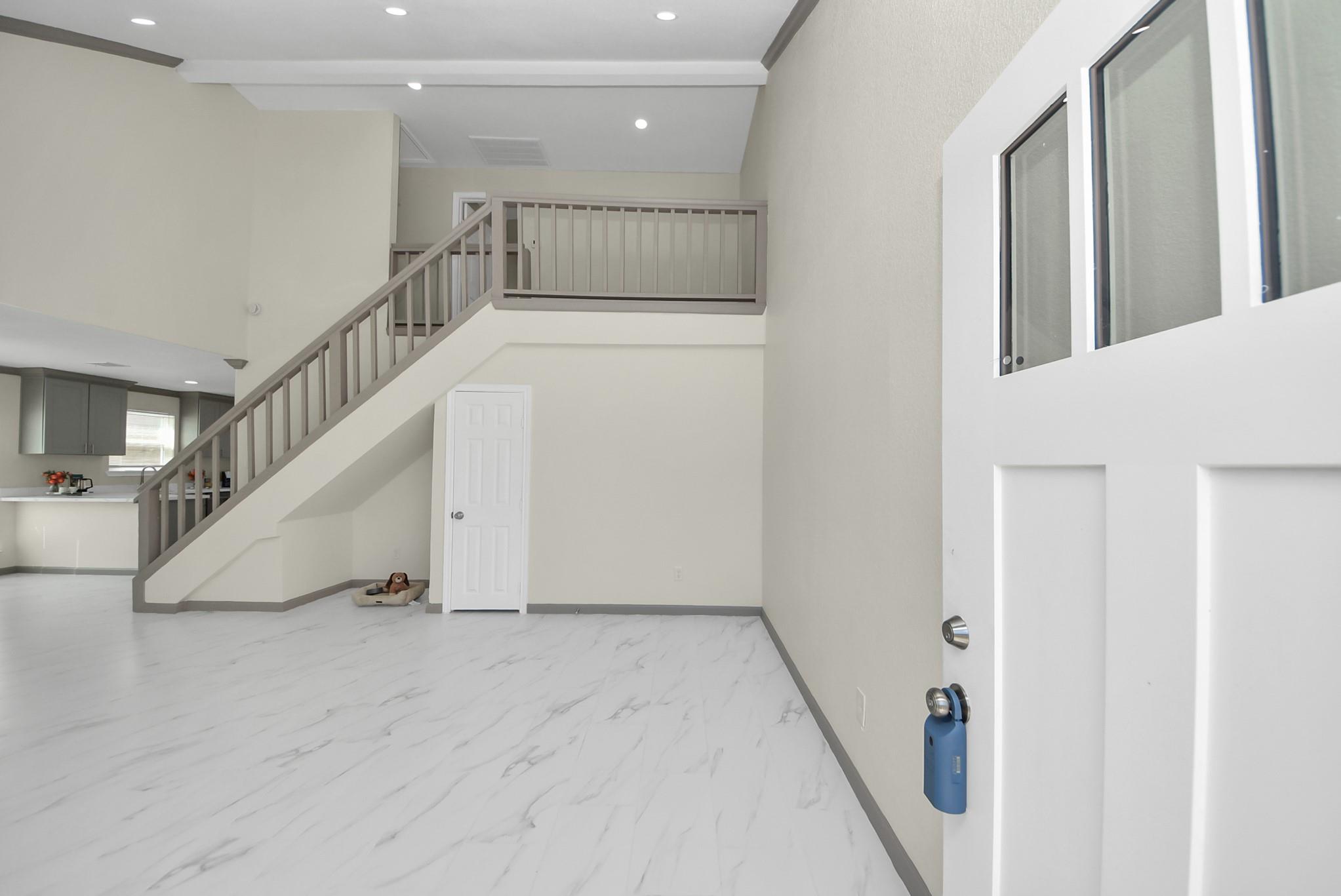 Two-story foyer with a gray-railed staircase, marble-look flooring, and an open view toward the kitchen.