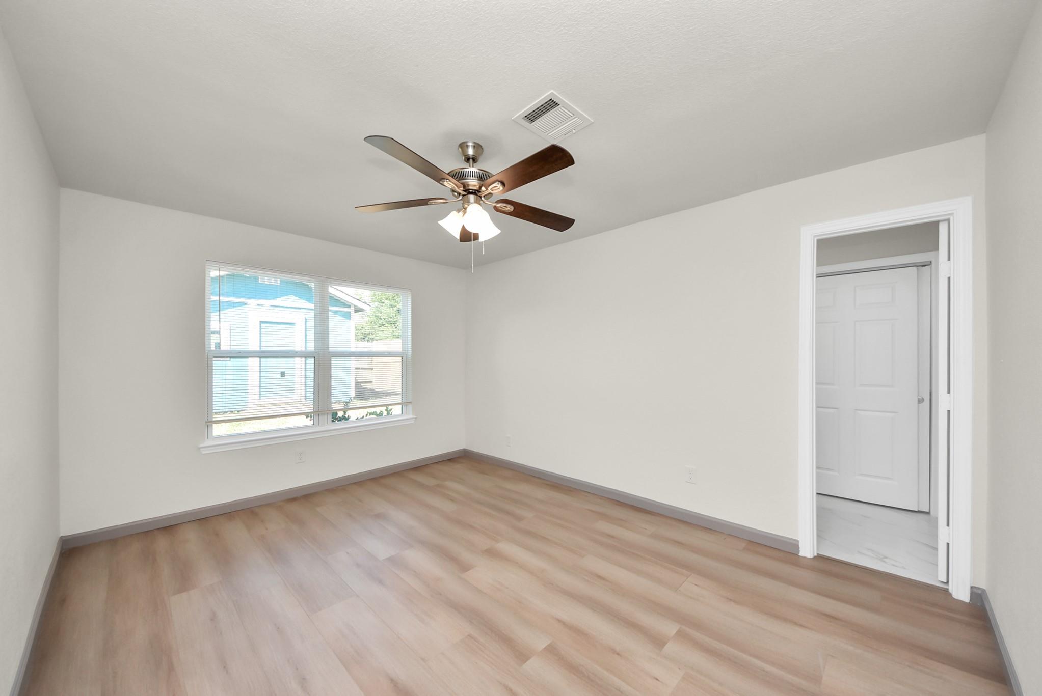 Vacant bedroom with light wood-look flooring, a ceiling fan, and a window with blinds.