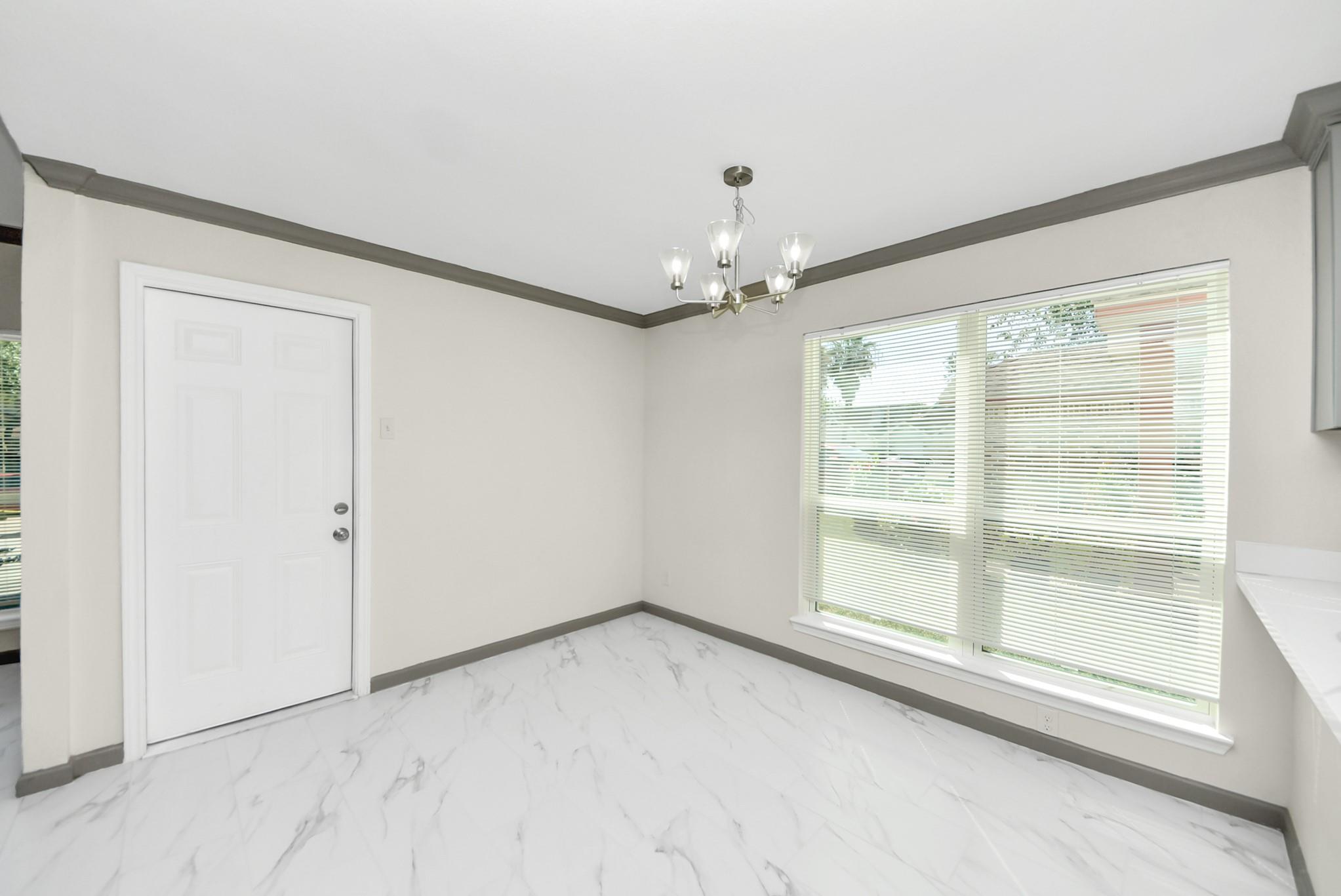 Empty room with marble-look tile floors, a chandelier, and a large window with blinds.